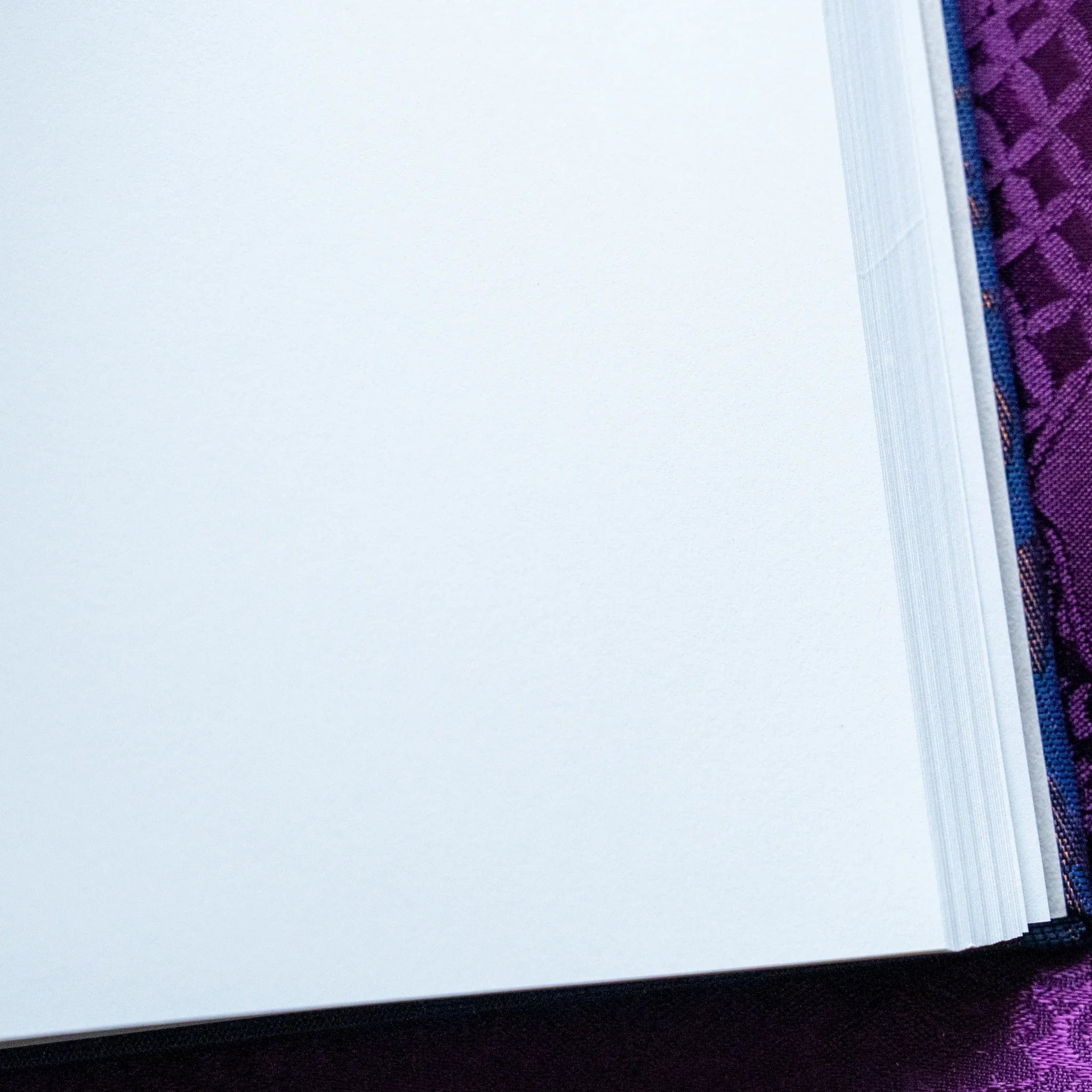 Oni Kiri Nishijin silk Homeicho notebook fore-edge close-up showing clean white page stack with dark navy cover on purple
