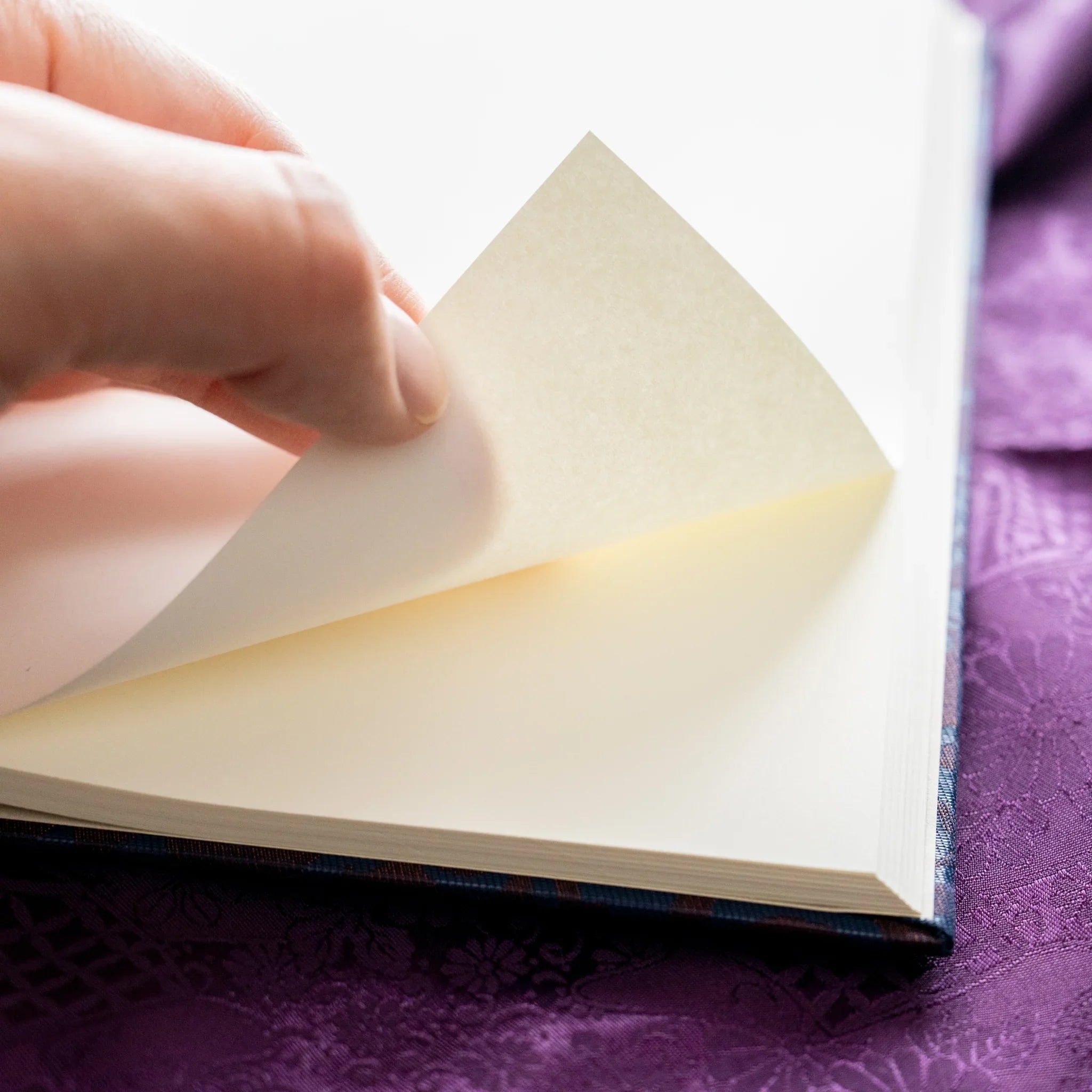 Hand turning page of Oni Kiri Nishijin silk Homeicho notebook showing smooth cream Rough Cream paper texture and navy cover