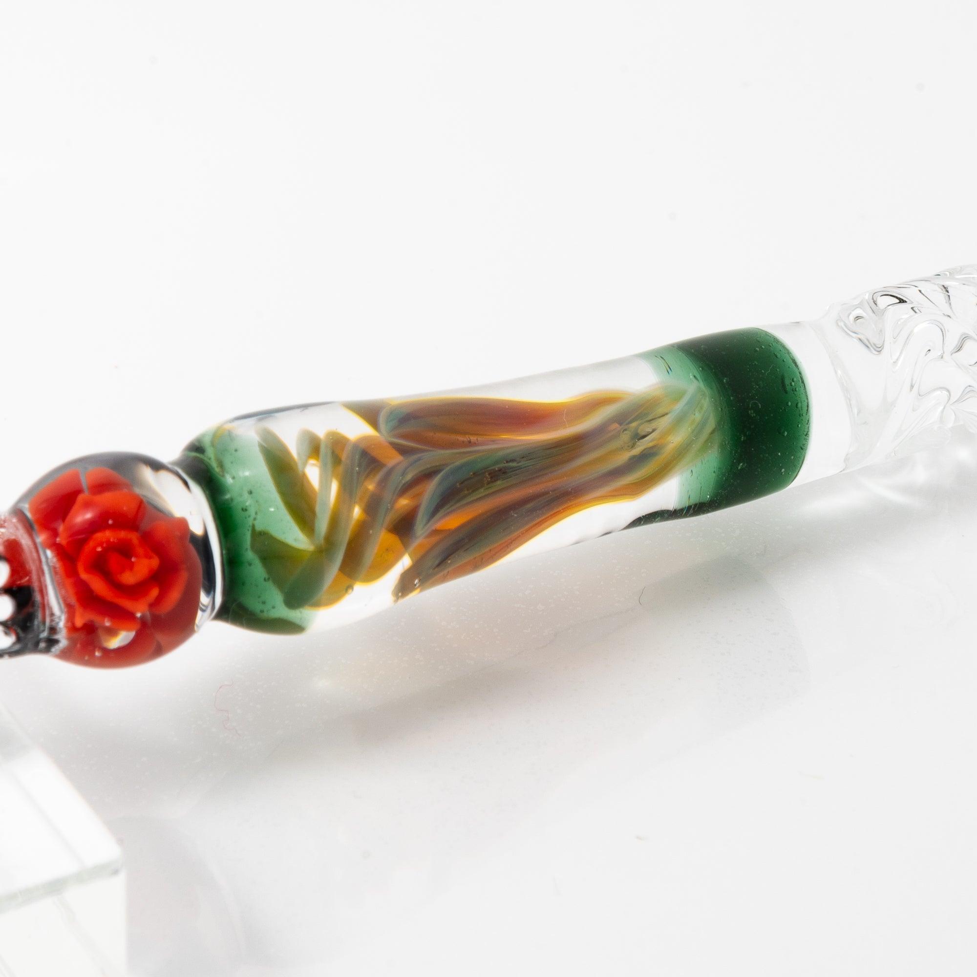 A delicate glass pen with an intricate orange rose motif, resting on a clear pen holder.