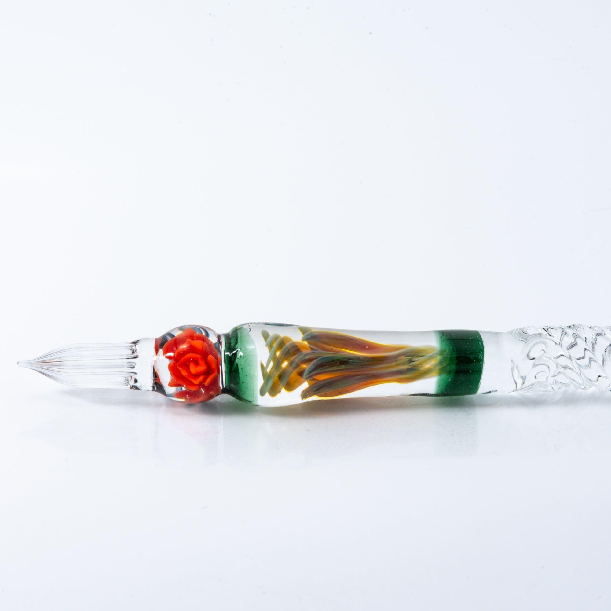 A delicate glass pen with an intricate orange rose motif, resting on a clear pen holder.