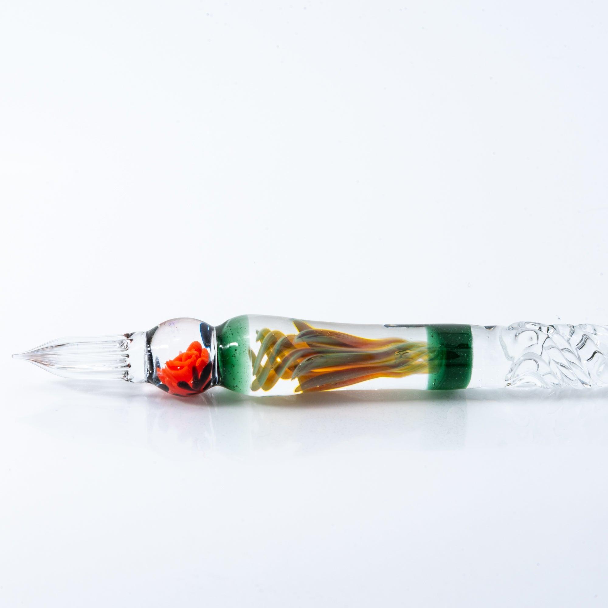 A delicate glass pen with an intricate orange rose motif, resting on a clear pen holder.