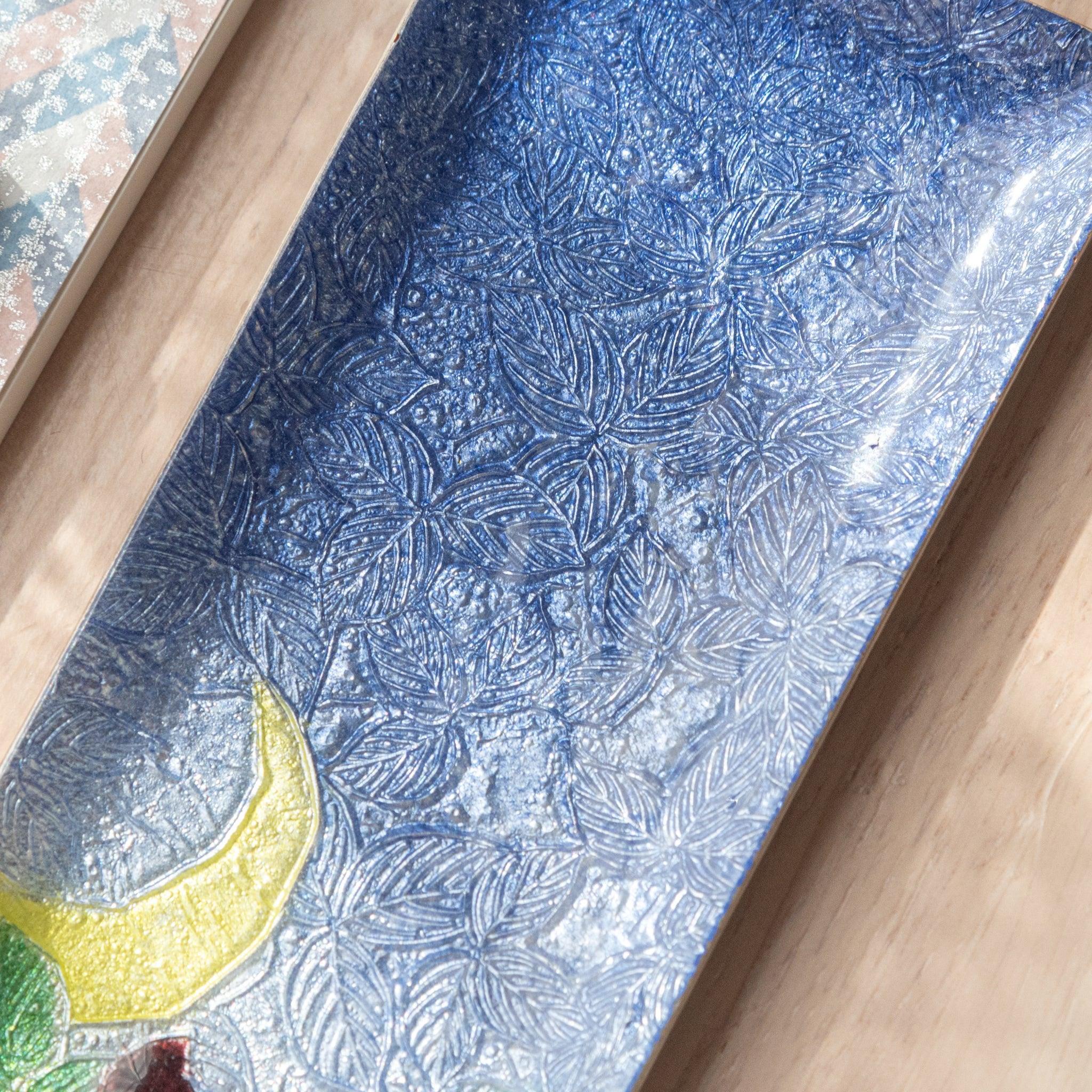 Close-up of a blue ceramic pen tray’s textured leaf pattern, showcasing intricate details and a yellow crescent moon in the design.