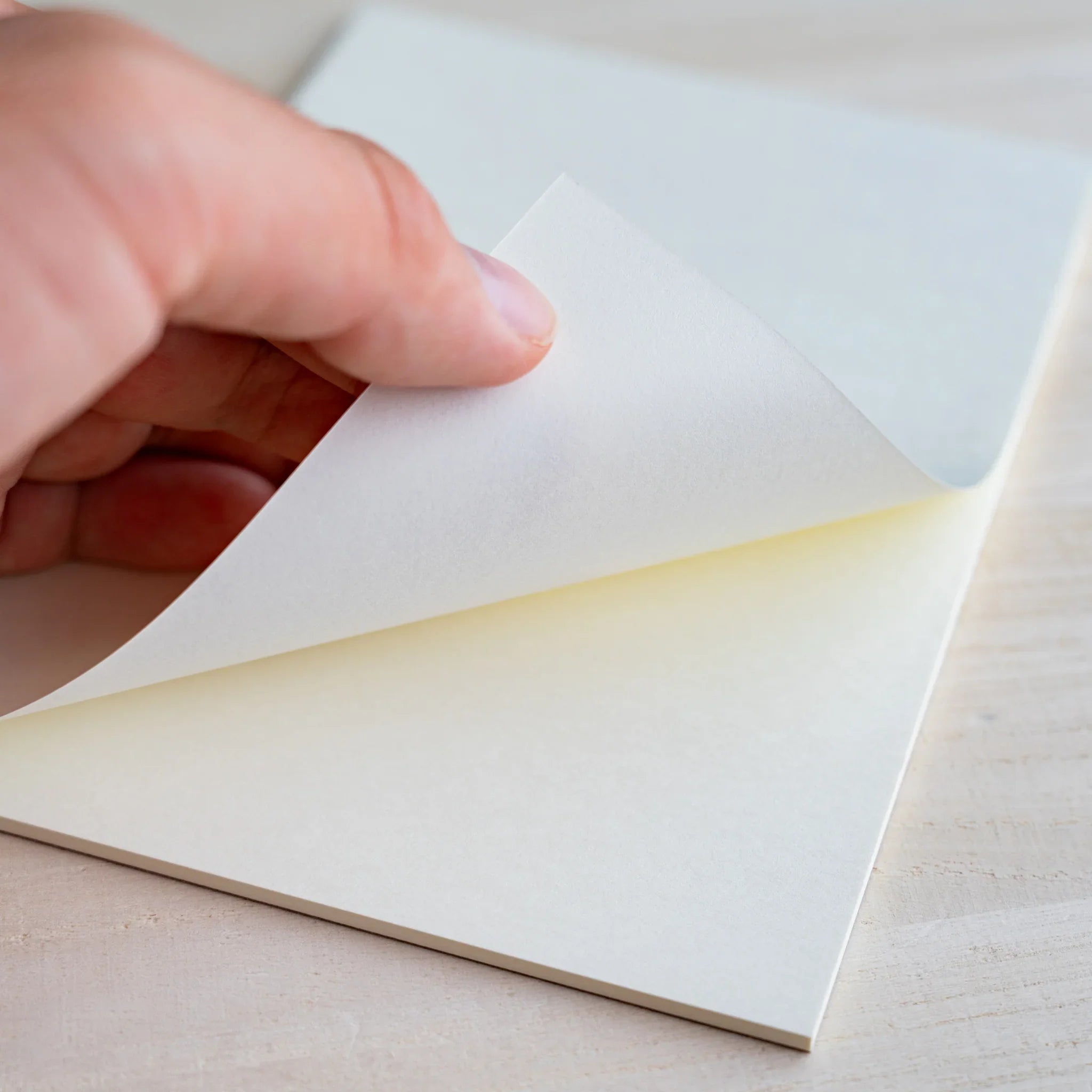 Hand lifting a white sheet to reveal a cream sheet beneath, showing different paper tones