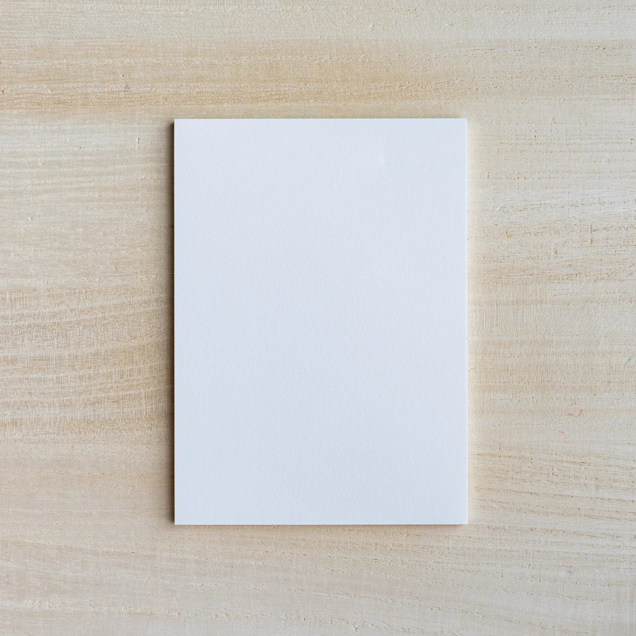 Single blank off-white eggshell-toned writing sheet on light wood surface