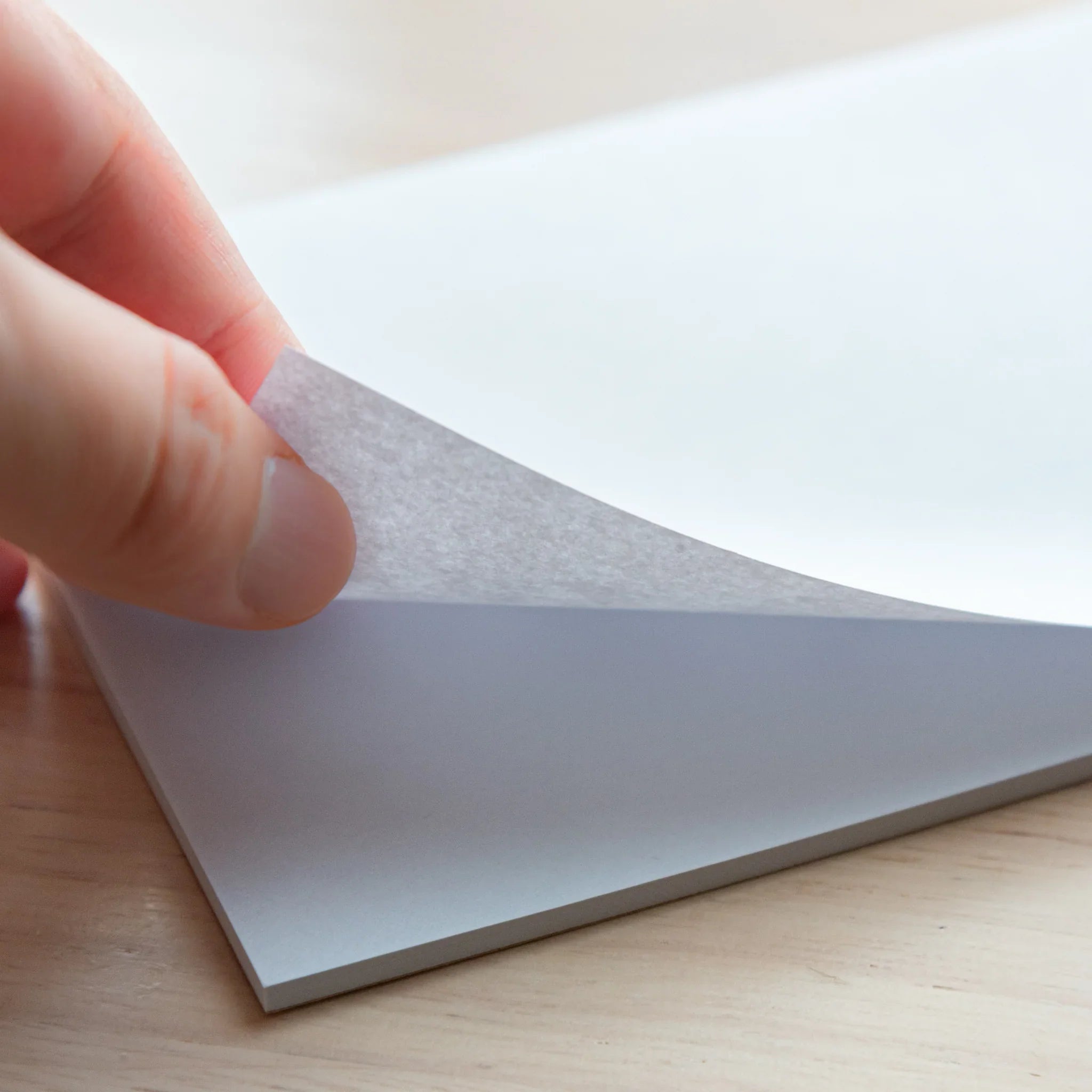 Hand lifting a sheet from the Paper Tasting Writing Pad Set – Gray vol.4, showing thin textured gray paper on a wooden desk.