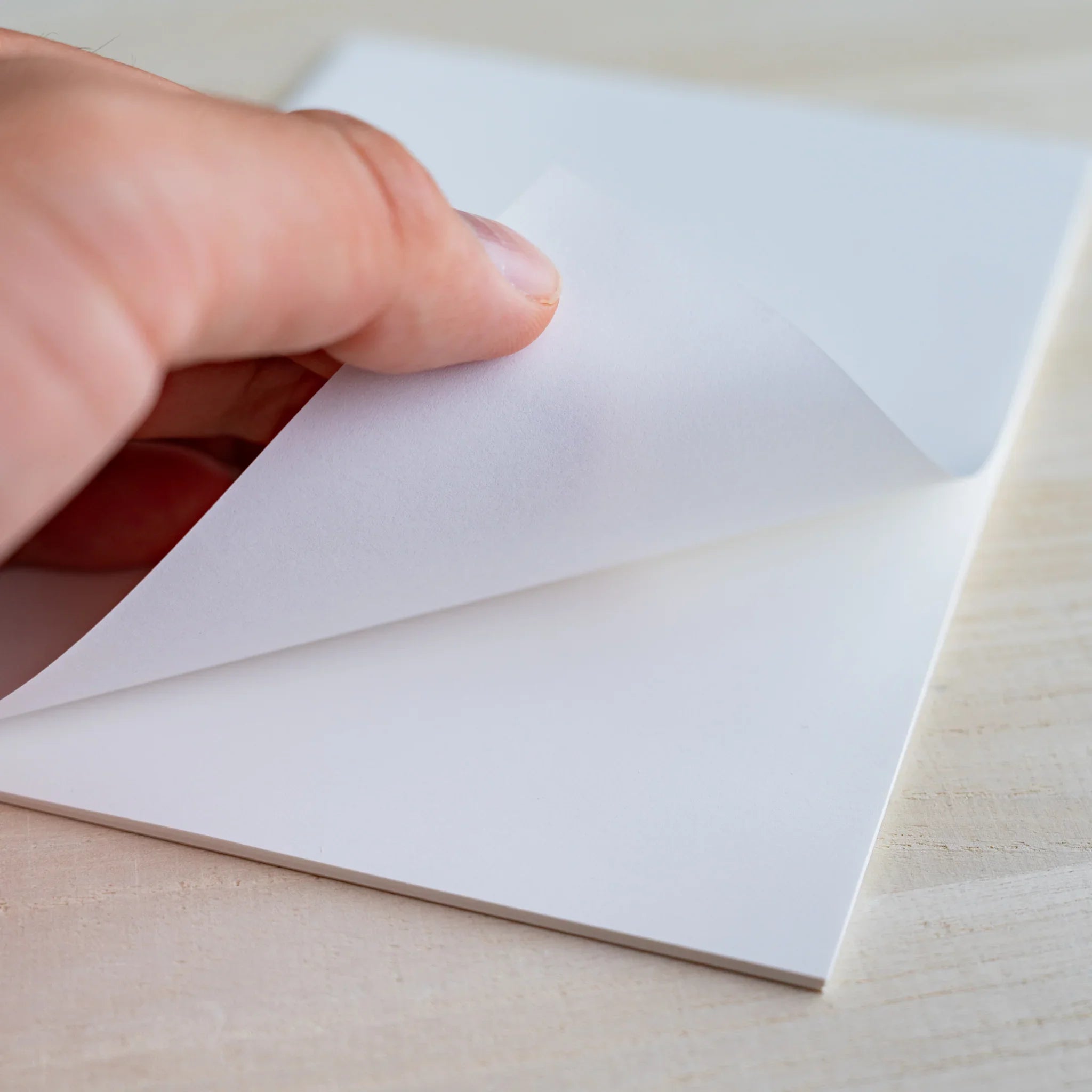 Fingers lifting a white sheet from the writing pad showing single-sheet thickness, on wood