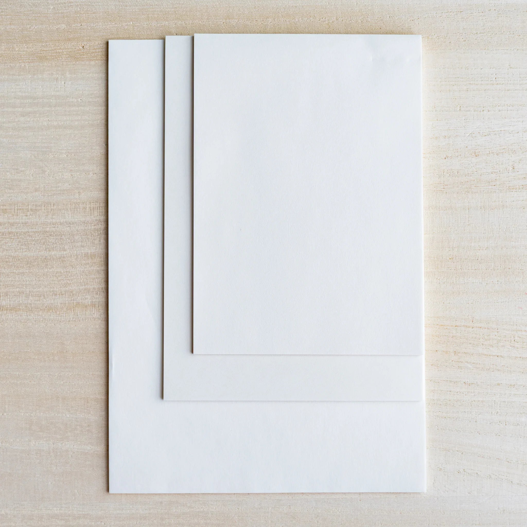 Three thin translucent white sample sheets stacked at different sizes on light wood