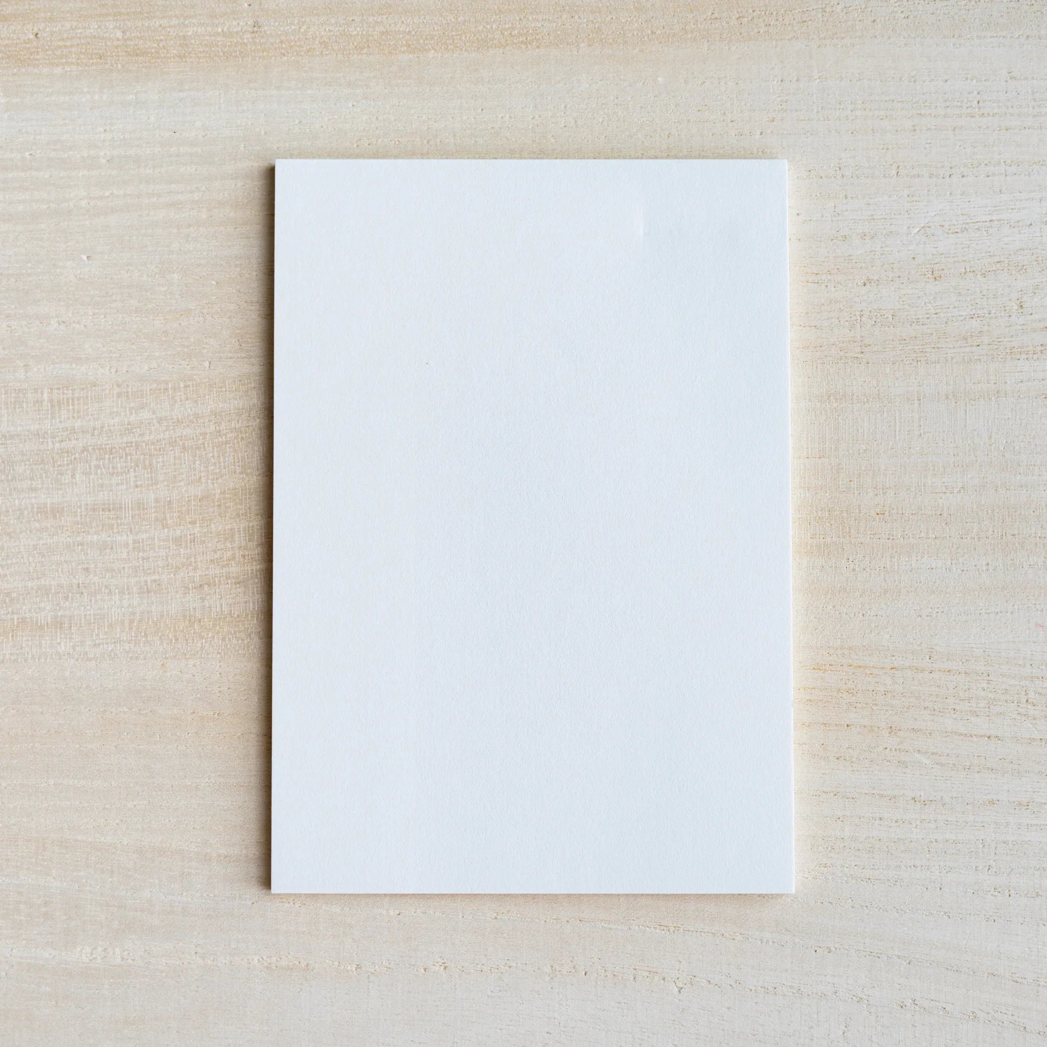 Single blank white silky-finish writing sheet on light wood surface
