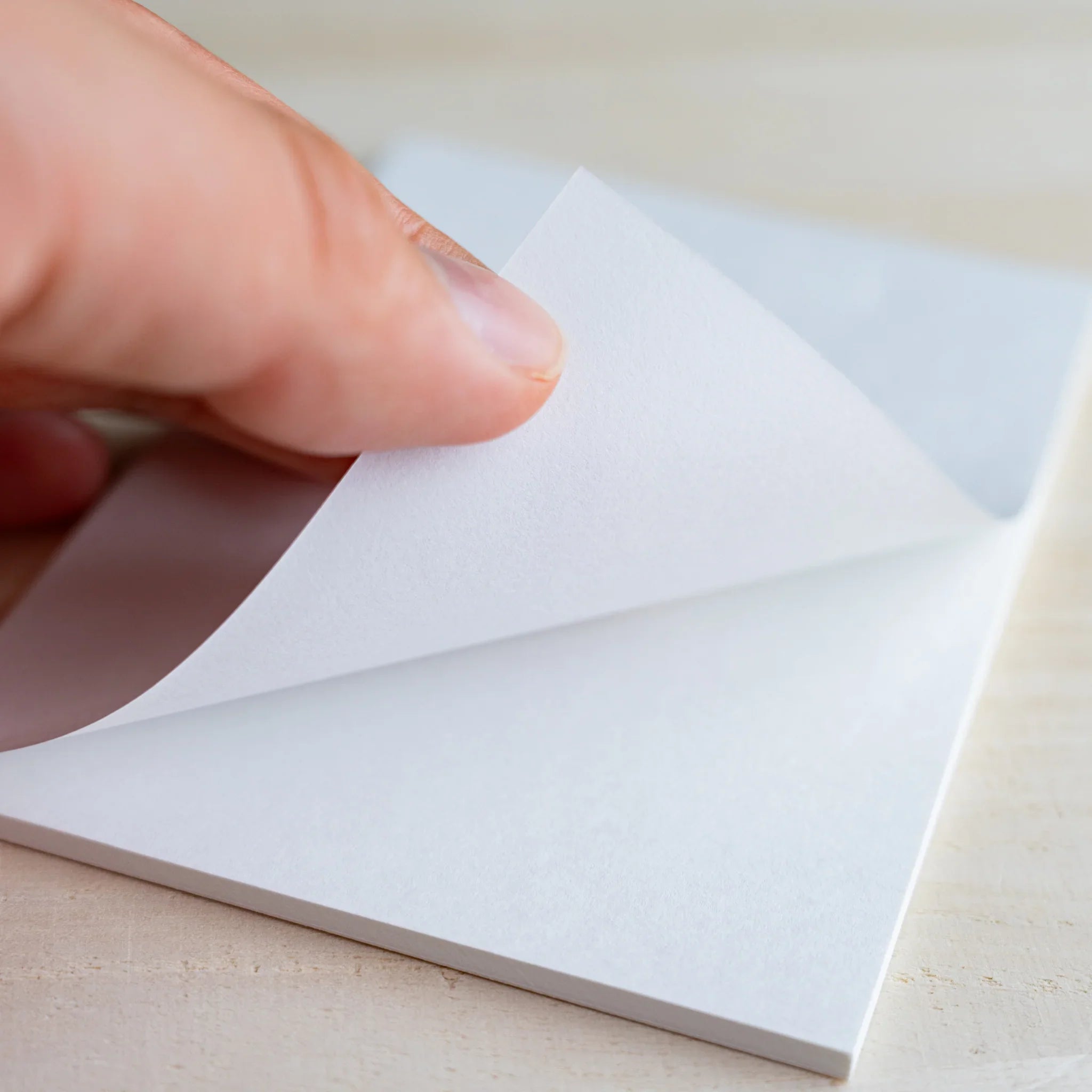 Hand lifting a smooth white sheet from the writing pad showing paper thickness, on wood