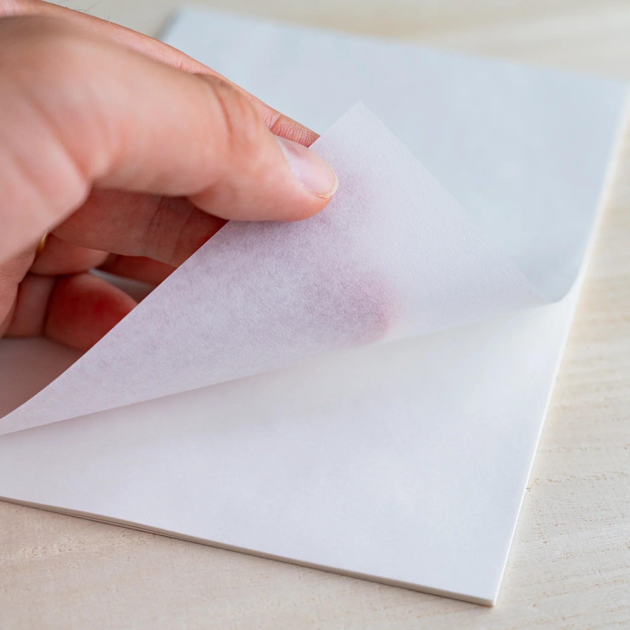 Hand lifting a translucent sheet showing the hand through the semi-transparent paper, on wood