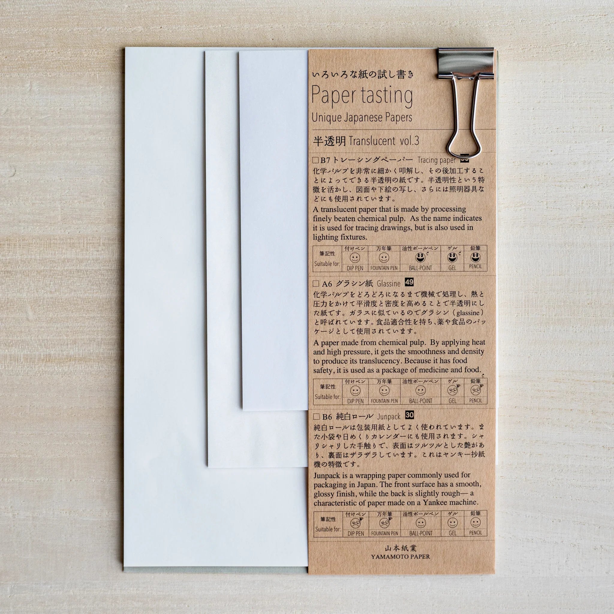 Paper tasting Translucent vol.3 set, semi-transparent sample sheets fanned beside kraft cover with binder clip on wood