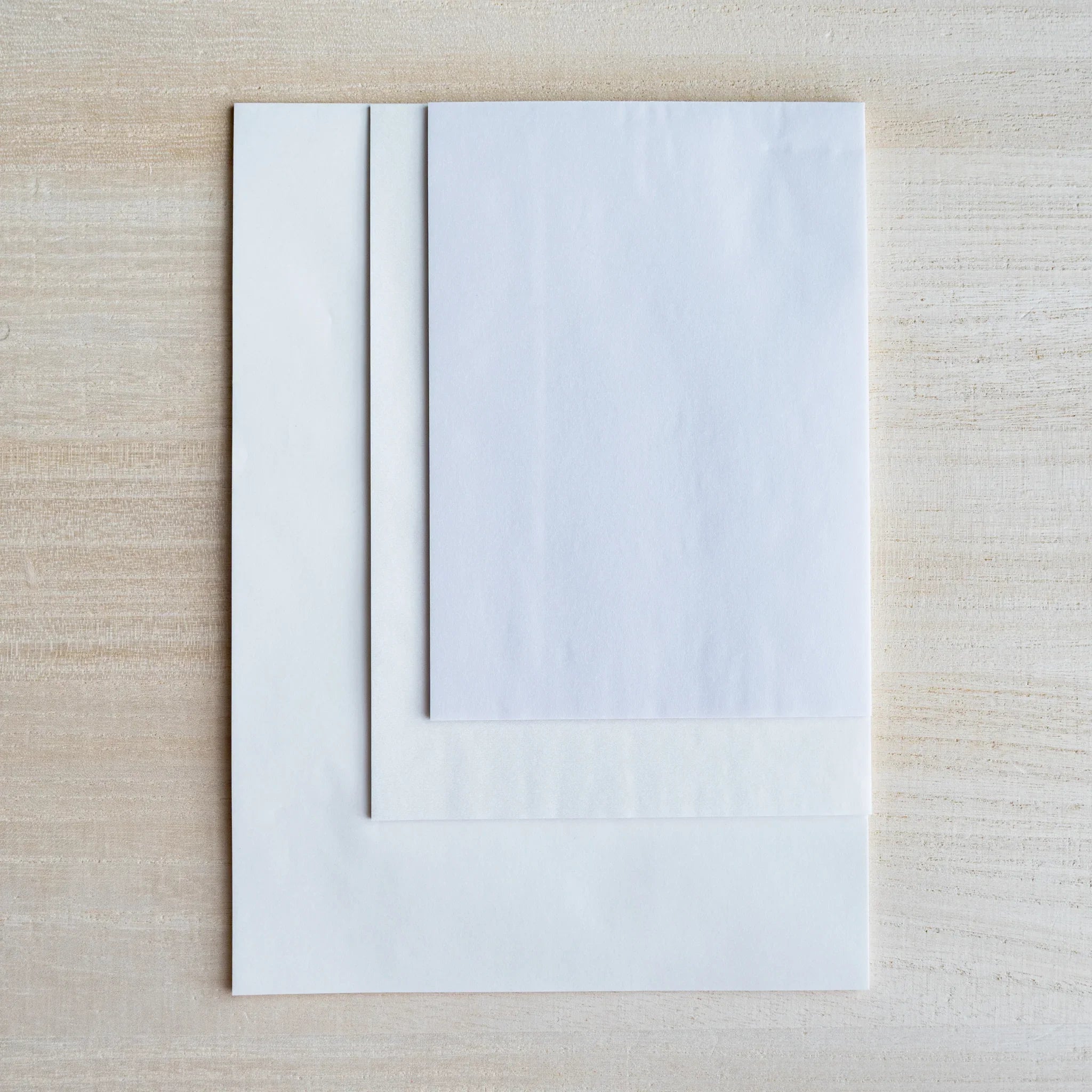 Three semi-transparent sample sheets stacked at different sizes, wood grain visible through them