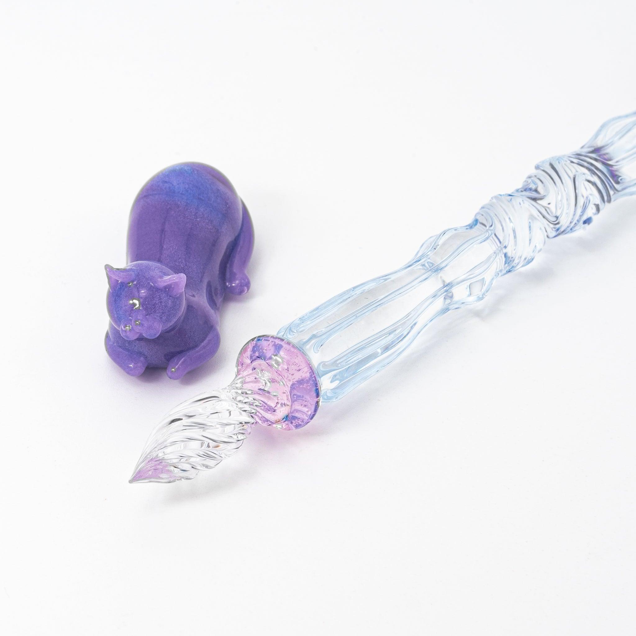 Glass pen with a blue shaft, purple cat topper, and pink charm. Includes matching purple pen rest. Perfect for Japanese stationery lovers.