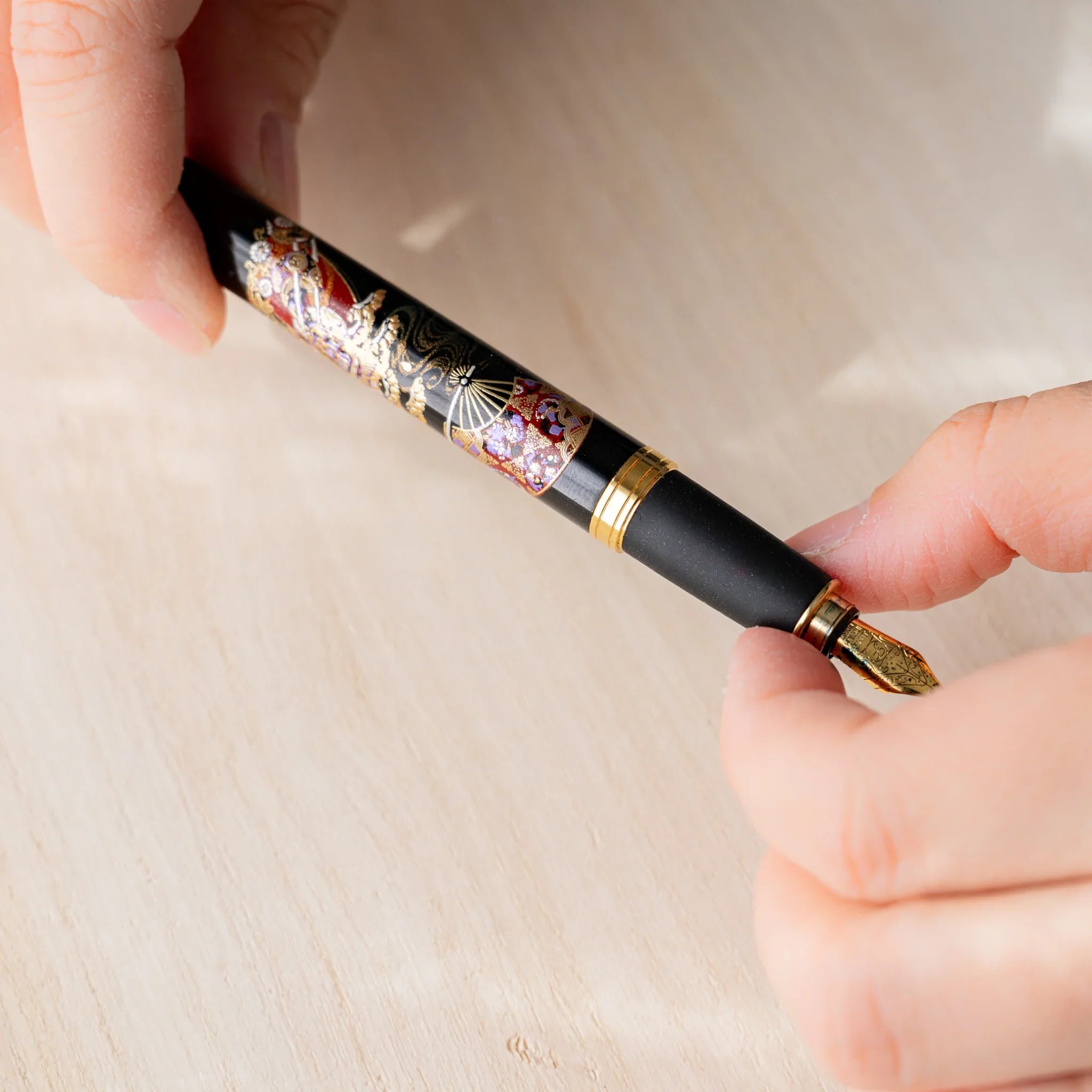 Hand holding a Yamanaka Japanese fountain pen with maki-e lacquer design showing the gold nib.