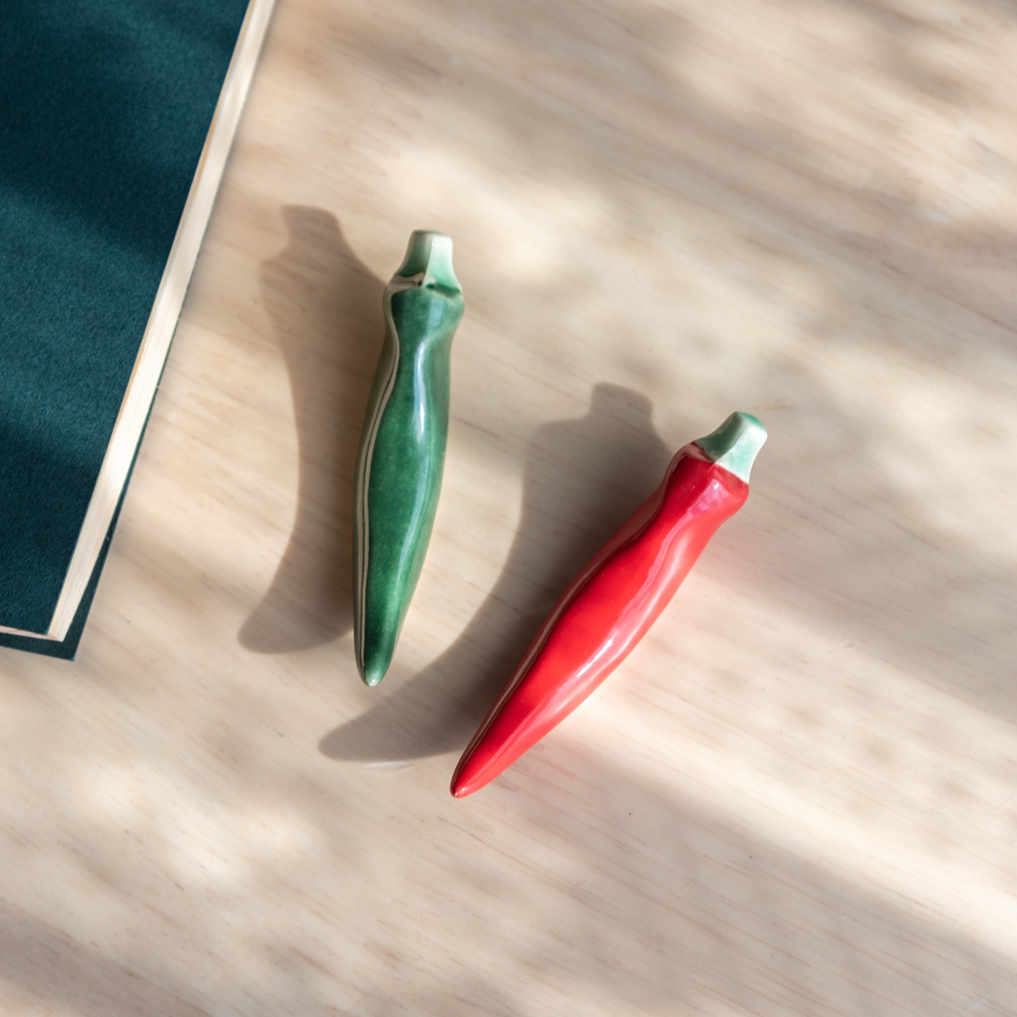 Handmade ceramic pen rests shaped as green and red chili peppers, part of Japanese stationery with a playful and vibrant design.