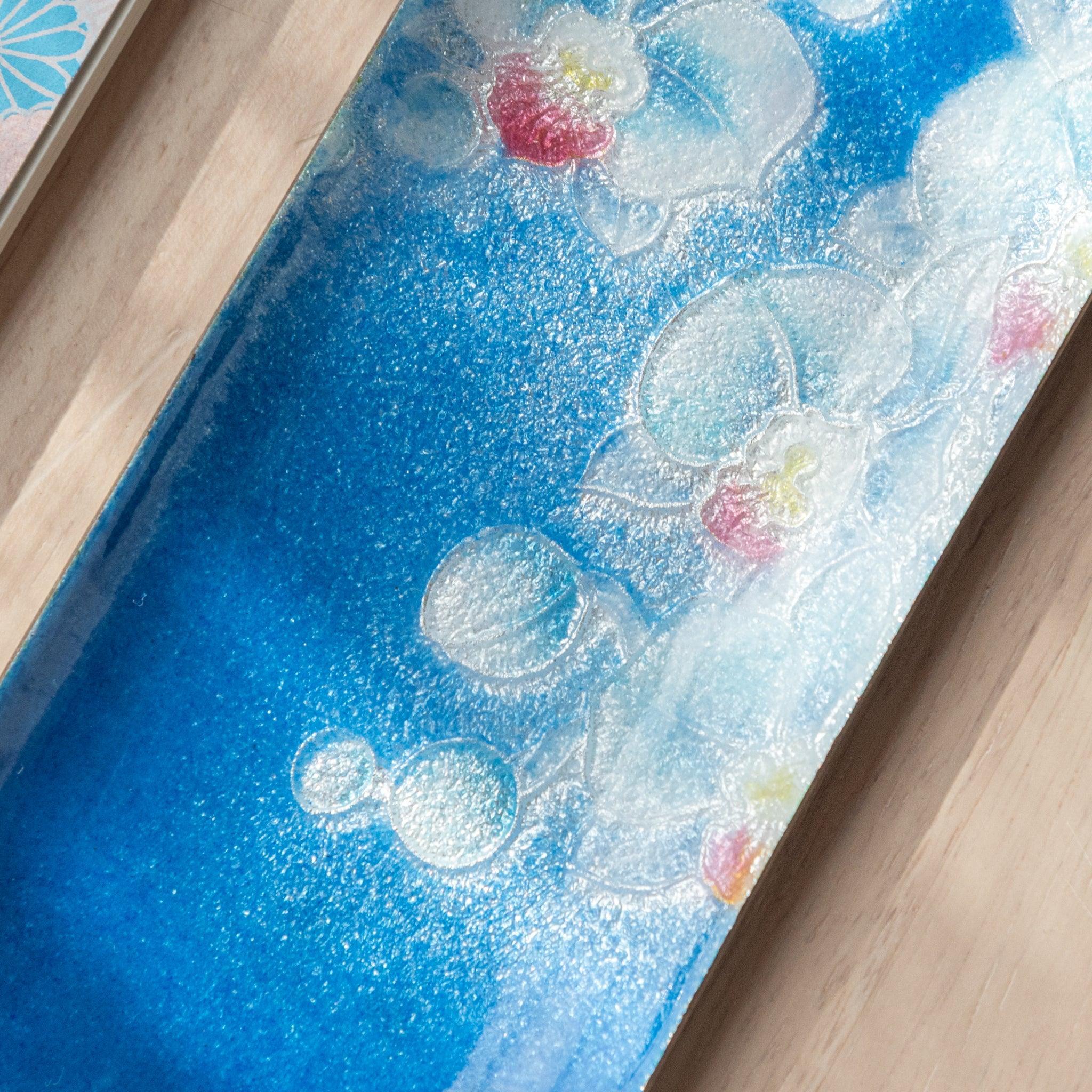 Detailed view of blue tray featuring orchid design with white petals and pink accents, highlighting intricate texture on a wooden background.