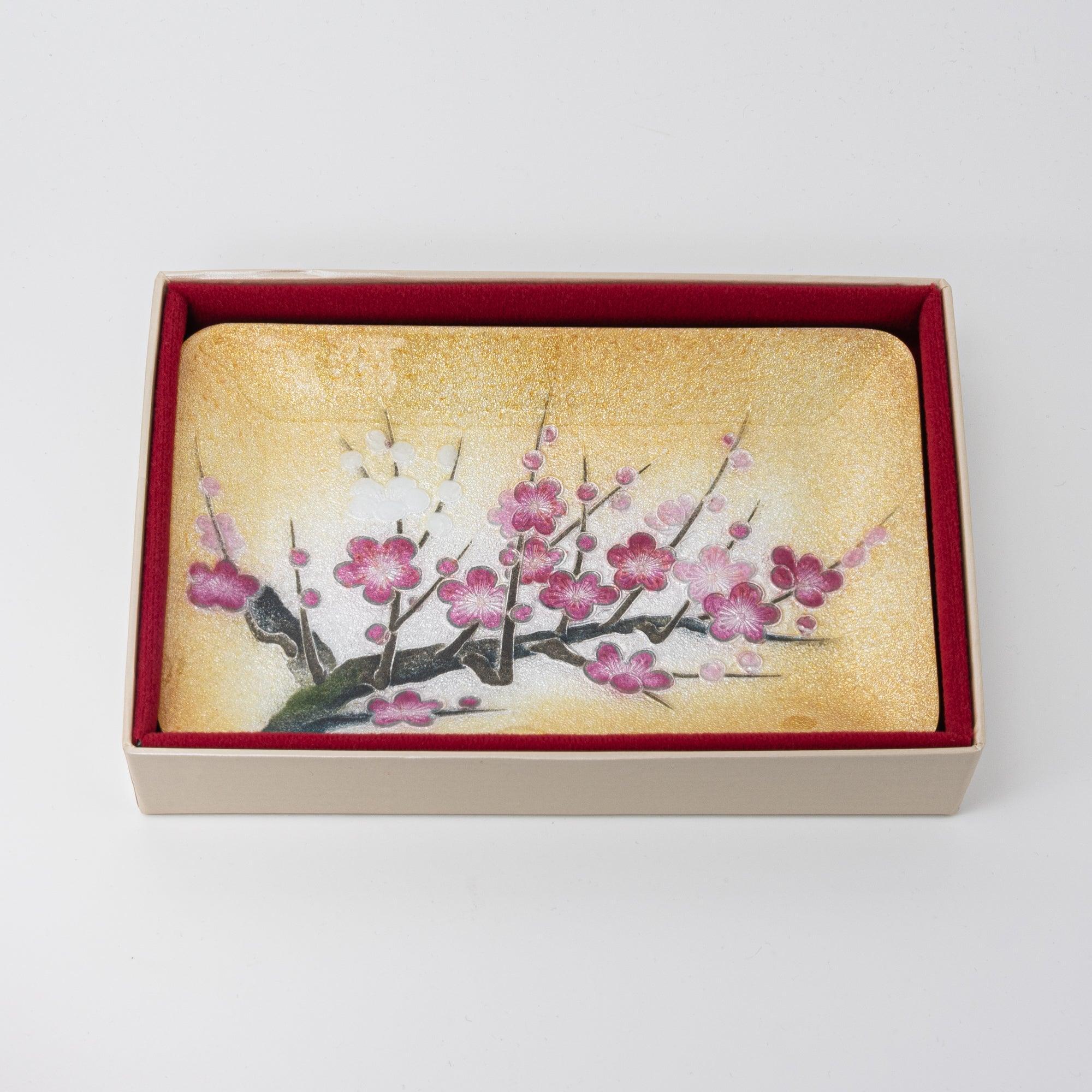 Golden tray with pink plum blossoms presented in a beige box lined with red fabric, combining elegance and protection.  