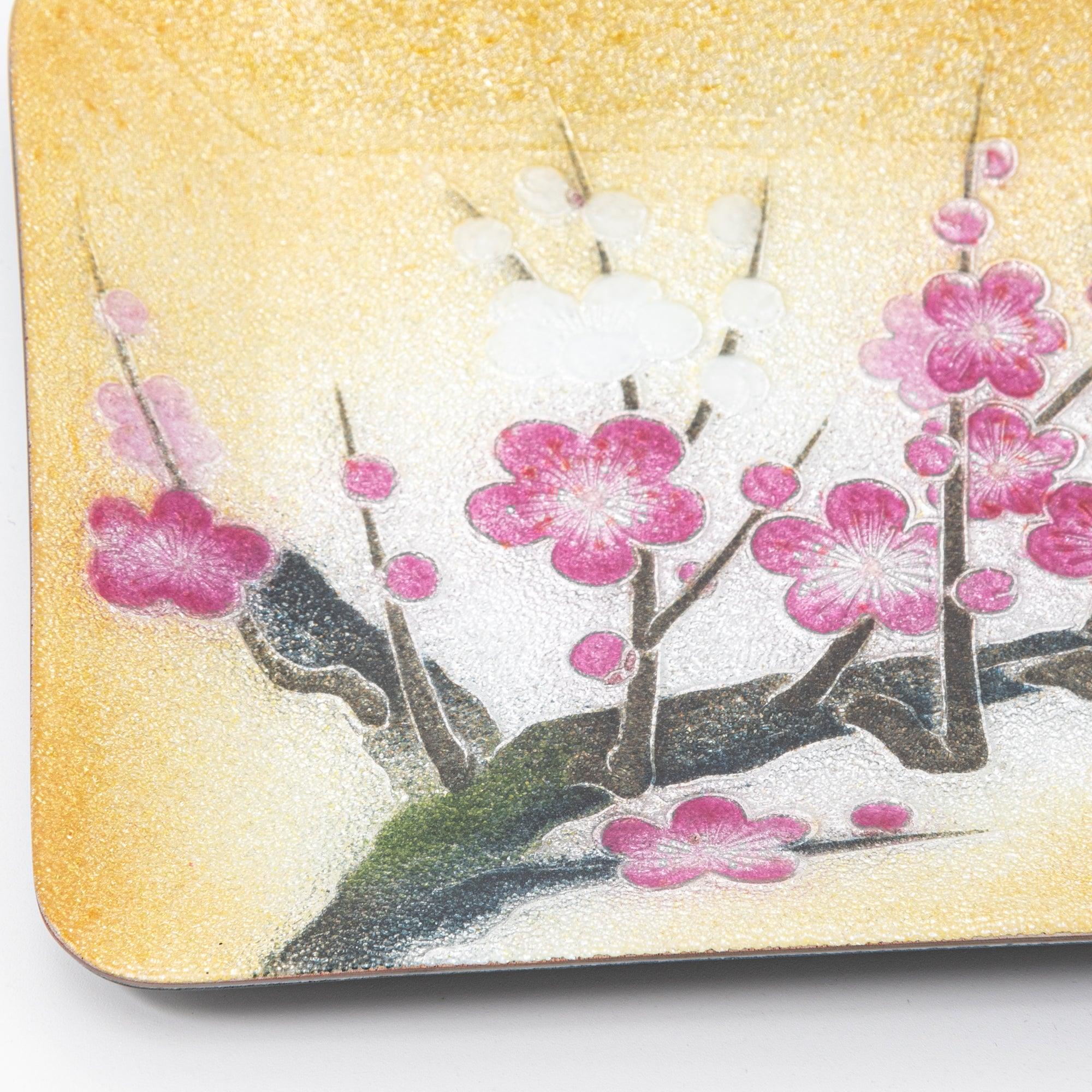 A close-up of a pink plum blossom design on a golden tray, showcasing the delicate details and texture of Japanese craftsmanship.  