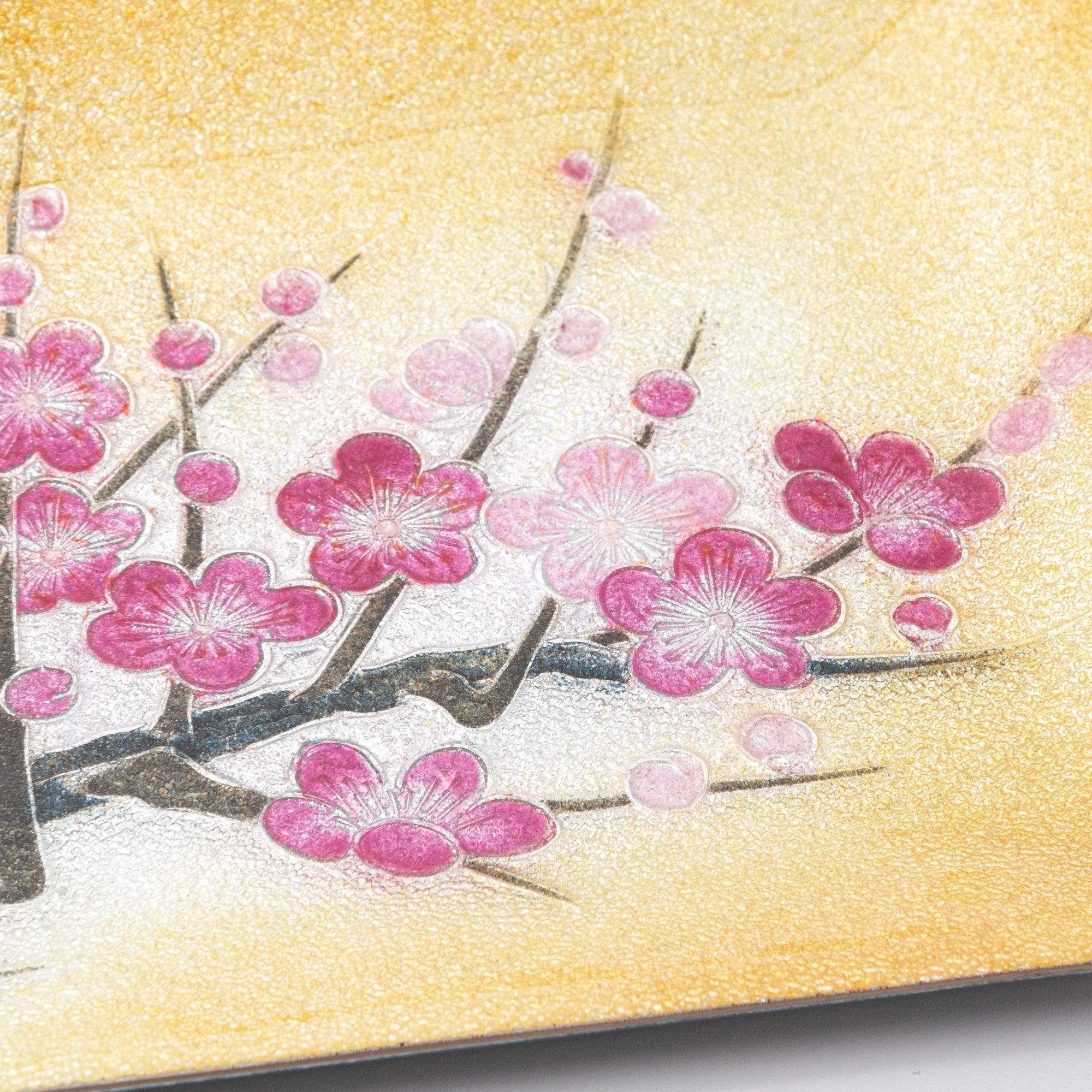 Close-up of pink plum blossoms on a textured golden tray, highlighting intricate floral details and delicate craftsmanship.  