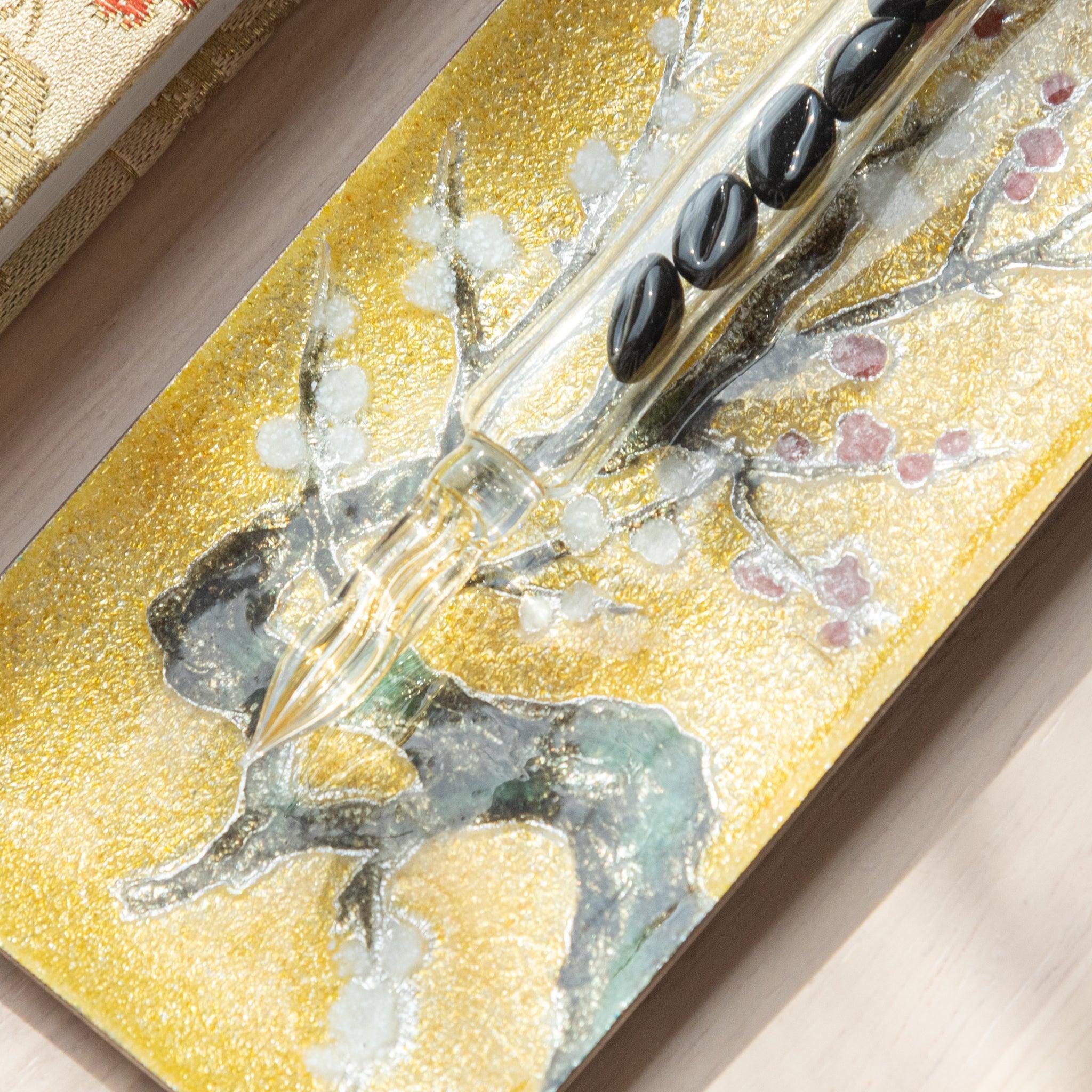 Angled view of gold tray with detailed plum blossom motif in white and red, placed beside a patterned fabric on a light wooden background.