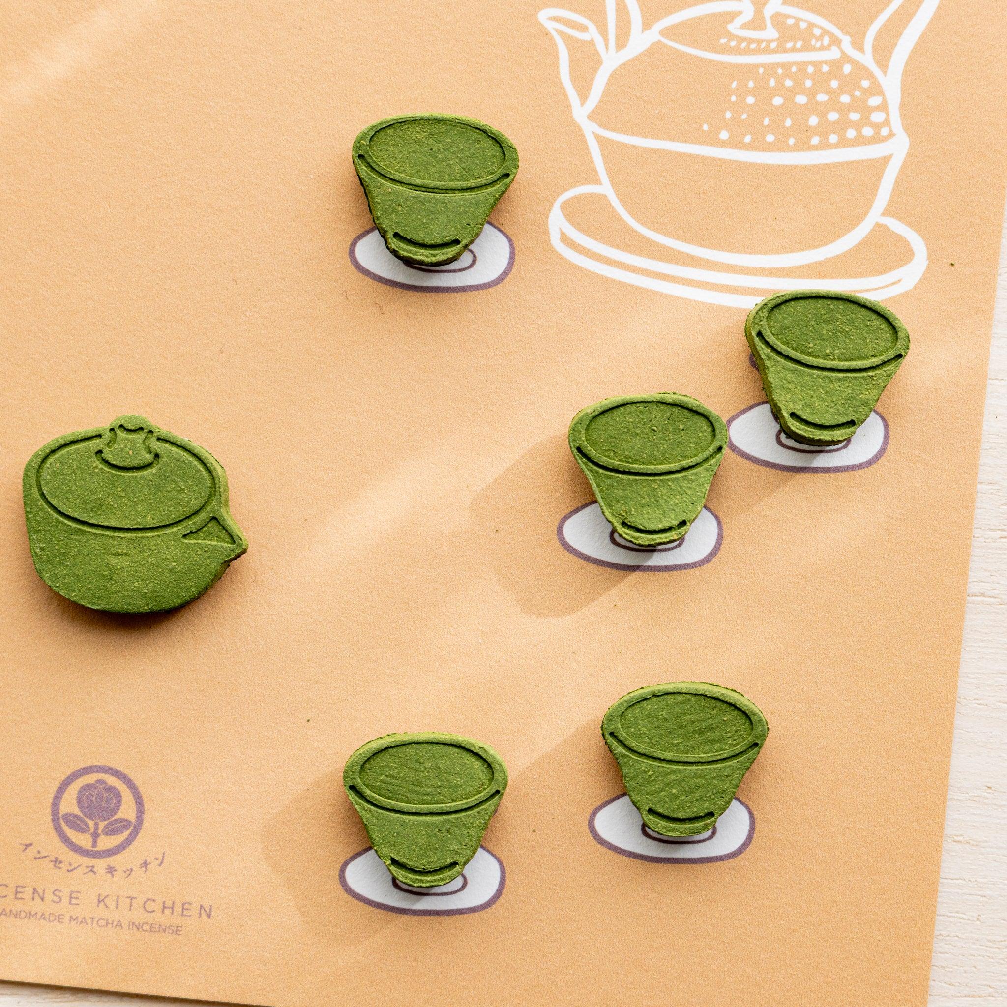 Close-up of tea variant pressed matcha incense card with green teapot and five tea cup pressed pieces on orange paper