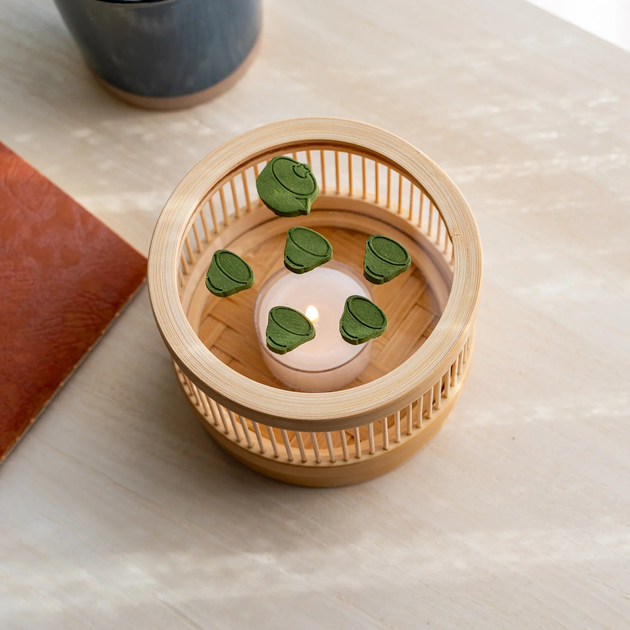 Bamboo matcha incense tea warmer from above with teapot and five tea cup pressed matcha pieces around a lit tealight