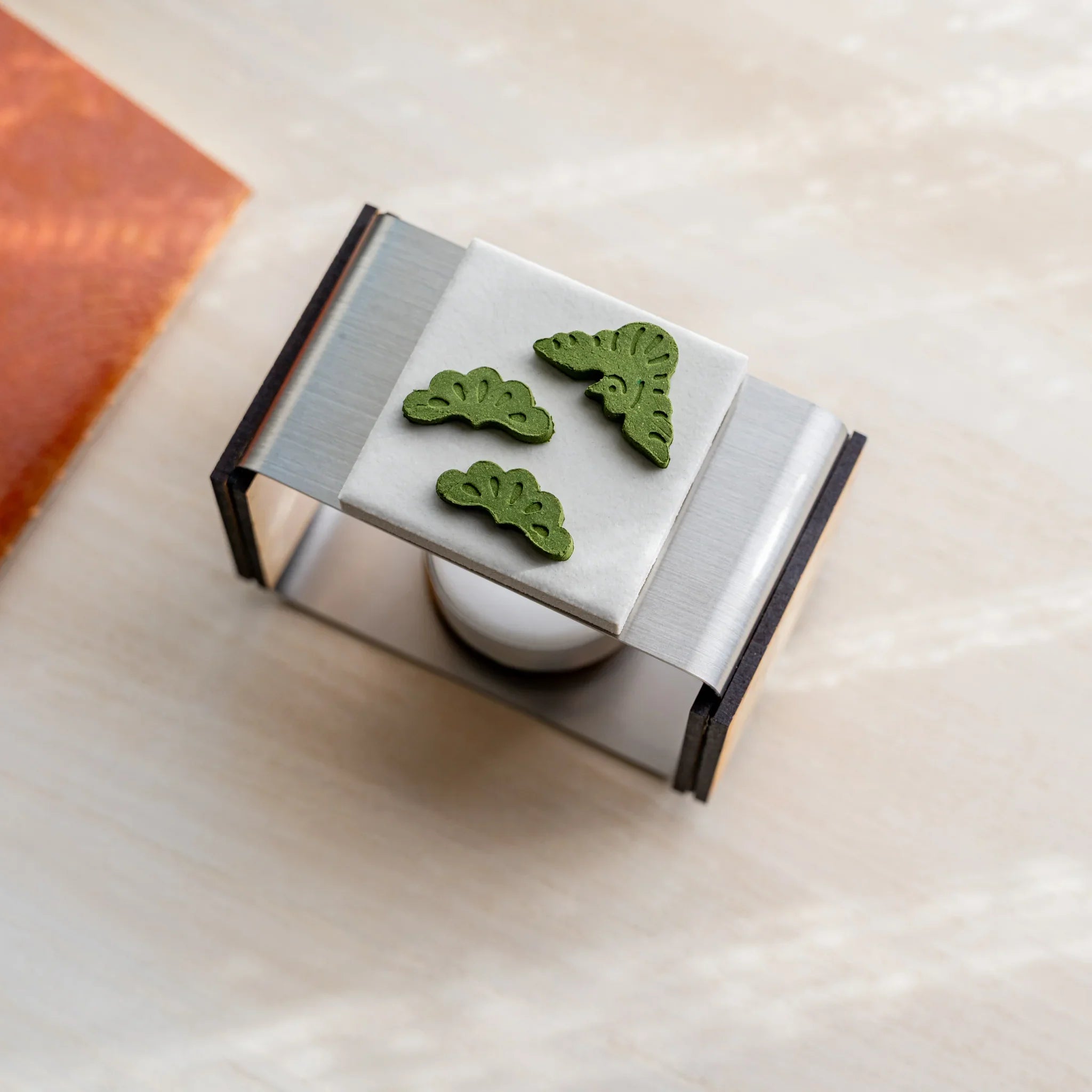 Top-down view of pine-sprig pressed matcha incense pieces on the ceramic plate of foldable matcha incense tea warmer