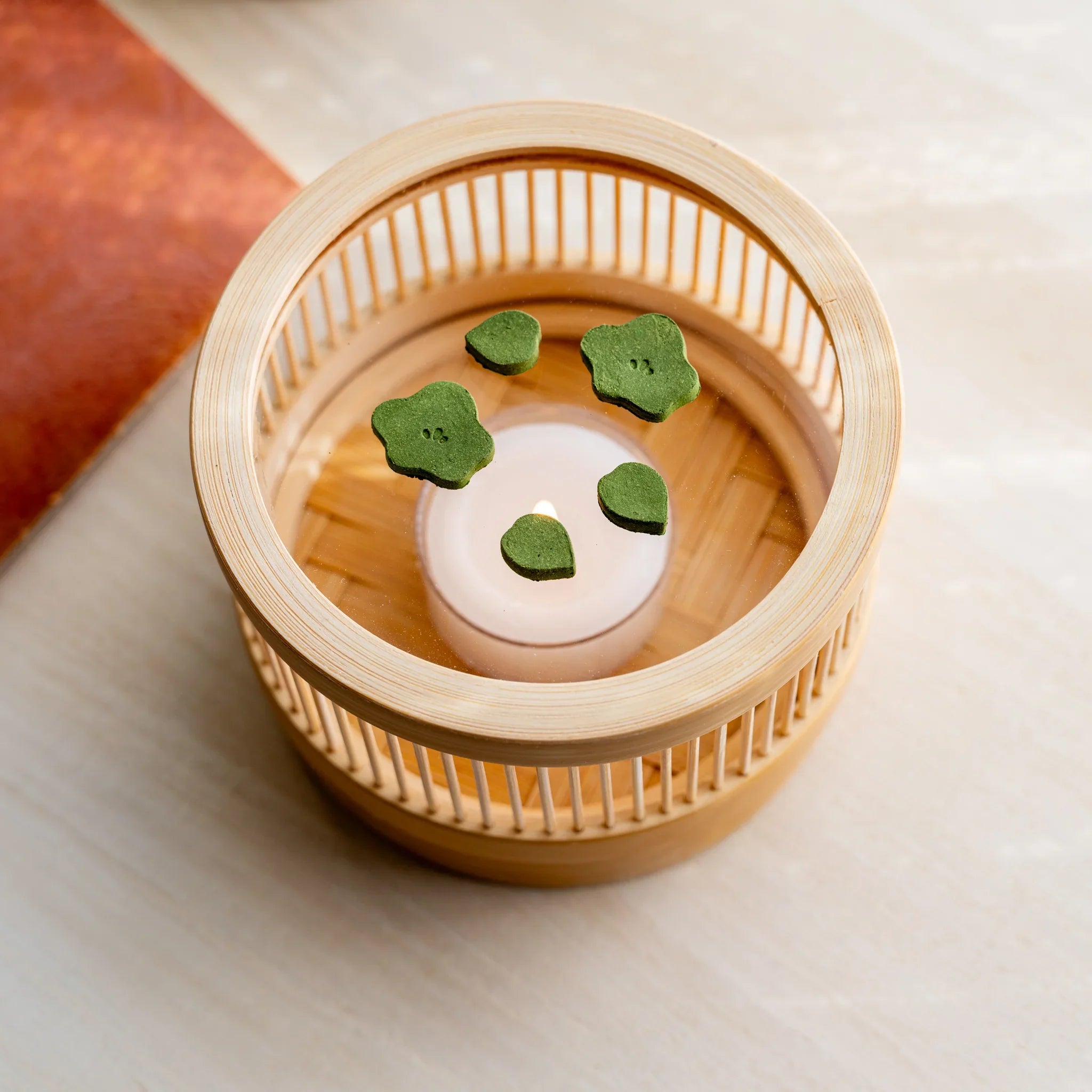 Three-quarter view of bamboo matcha incense tea warmer with plum-shape pressed matcha pieces and lit tealight