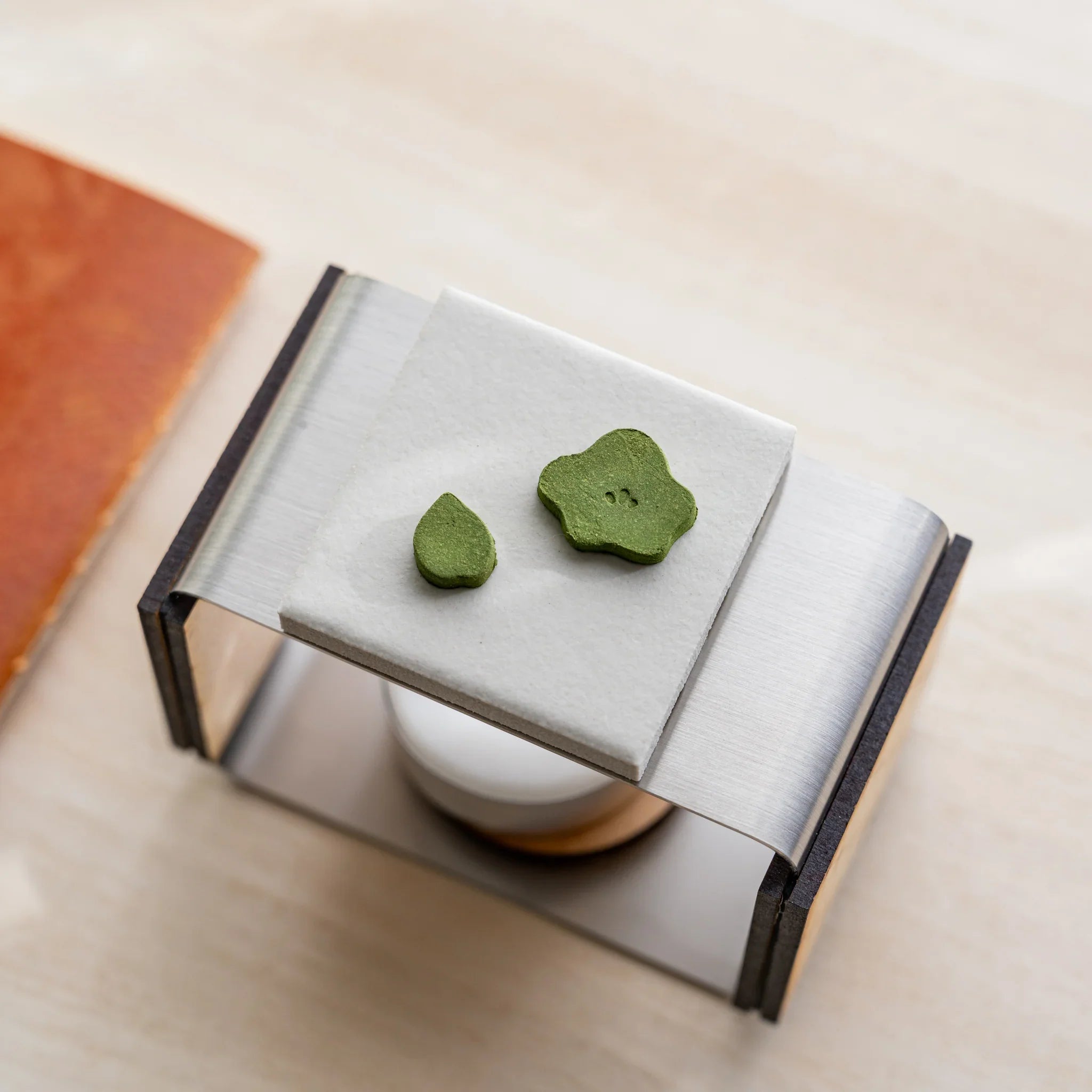 Close-up of two plum-shape pressed matcha incense pieces on the ceramic plate of foldable matcha incense tea warmer