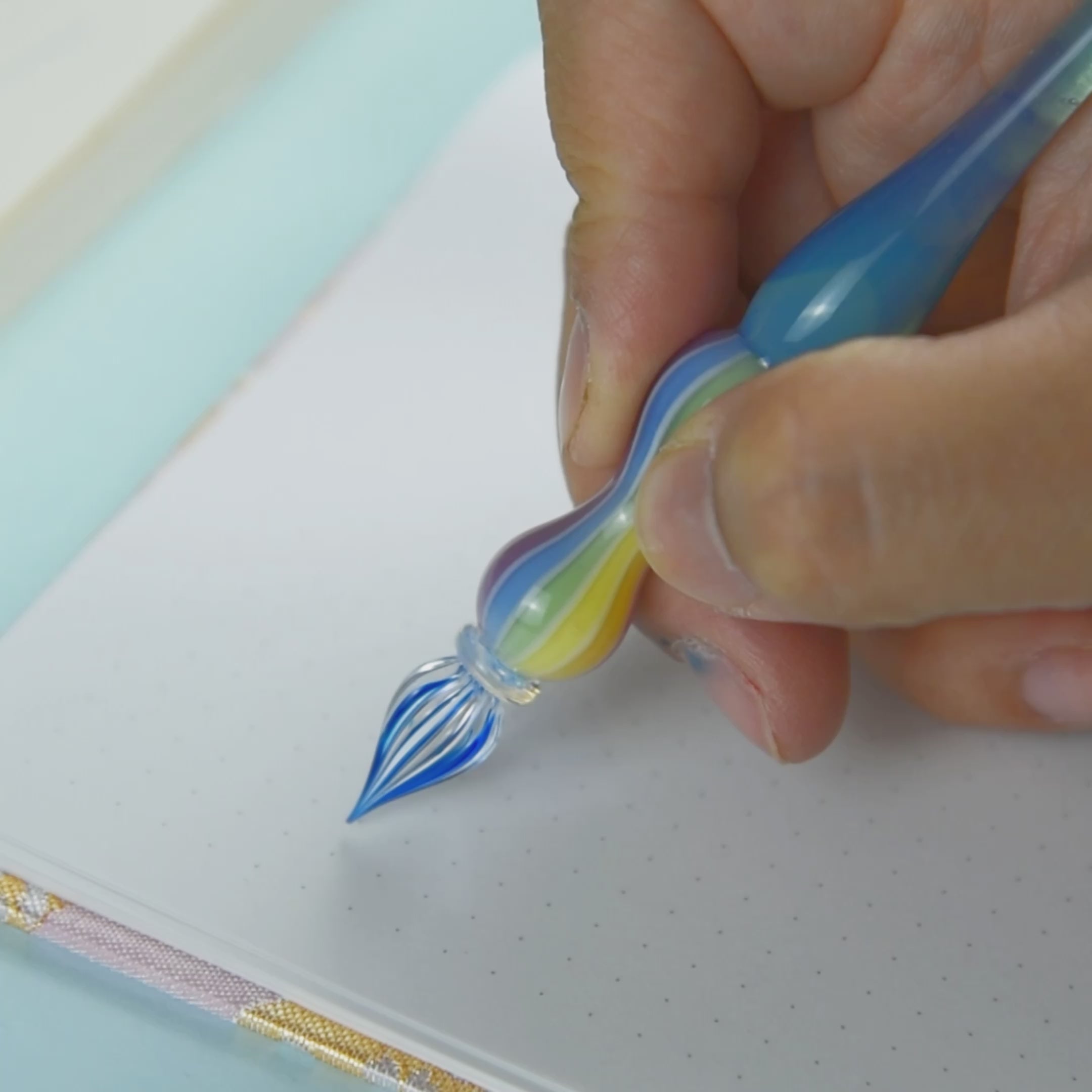 Rainbow-colored glass pen resting on a clear glass pen rest with blue starfish and seashell decor. Perfect for Japanese stationery enthusiasts.