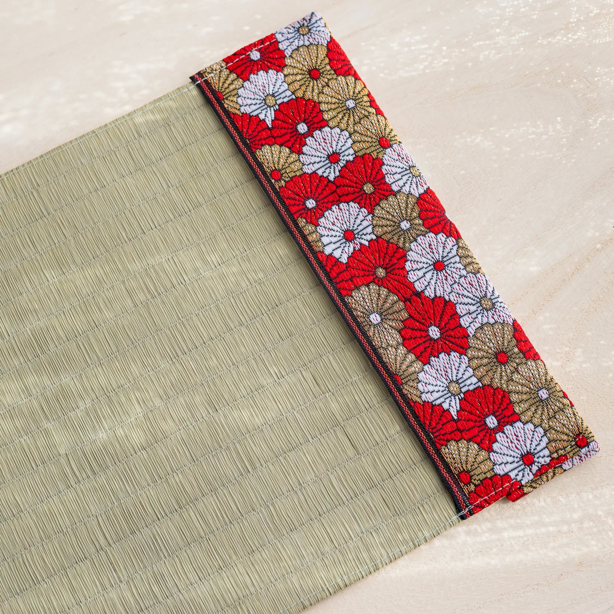 Diagonal view of tatami book cover edge, green rush straw with red white and gold chrysanthemum fabric band