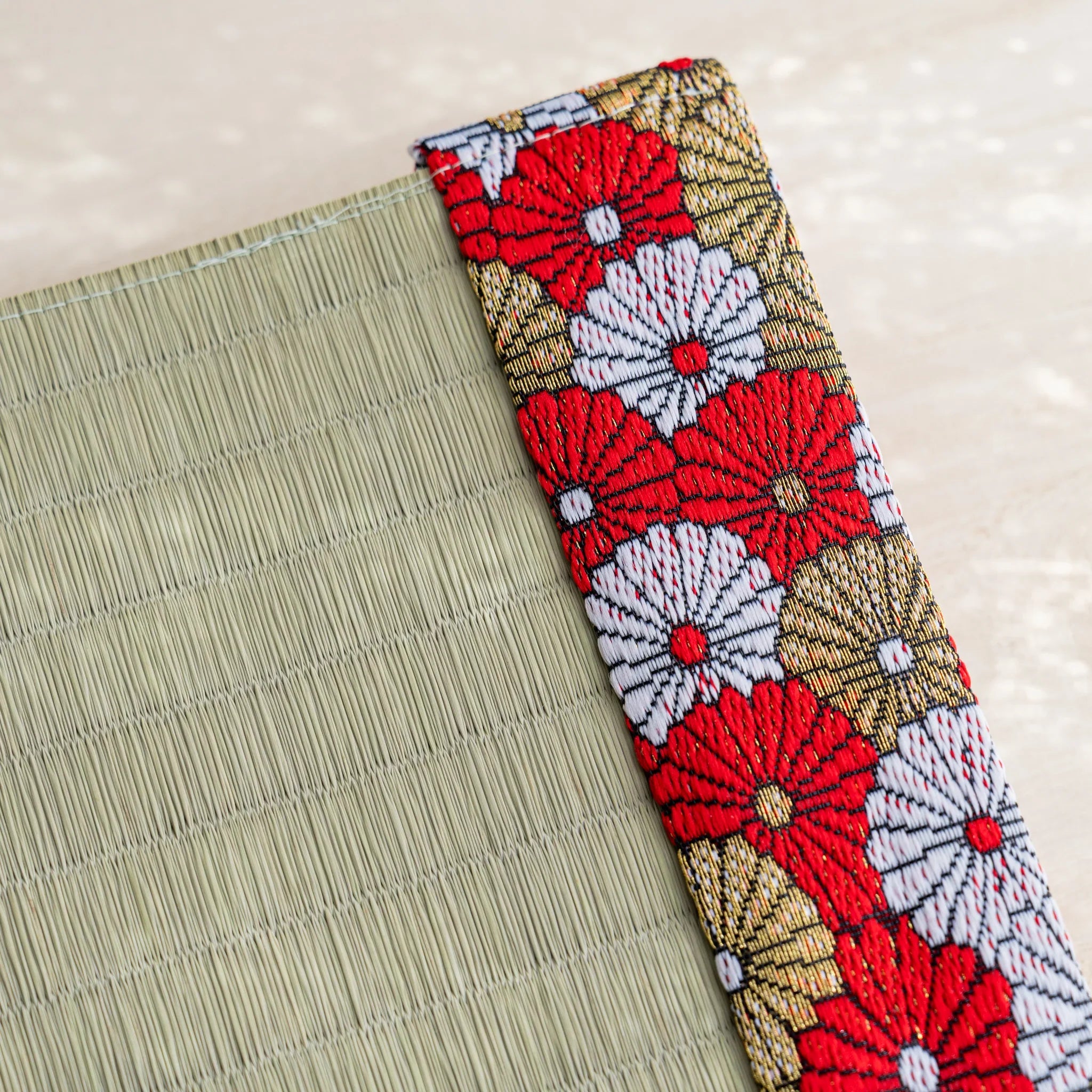 Close-up of red white and gold Japanese chrysanthemum brocade band beside woven green rush straw at the cover corner