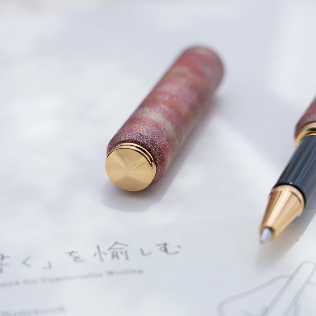 Red marbled urushi lacquered rollerball pen in zelkova wood with the cap removed, showing the barrel and gold trim
