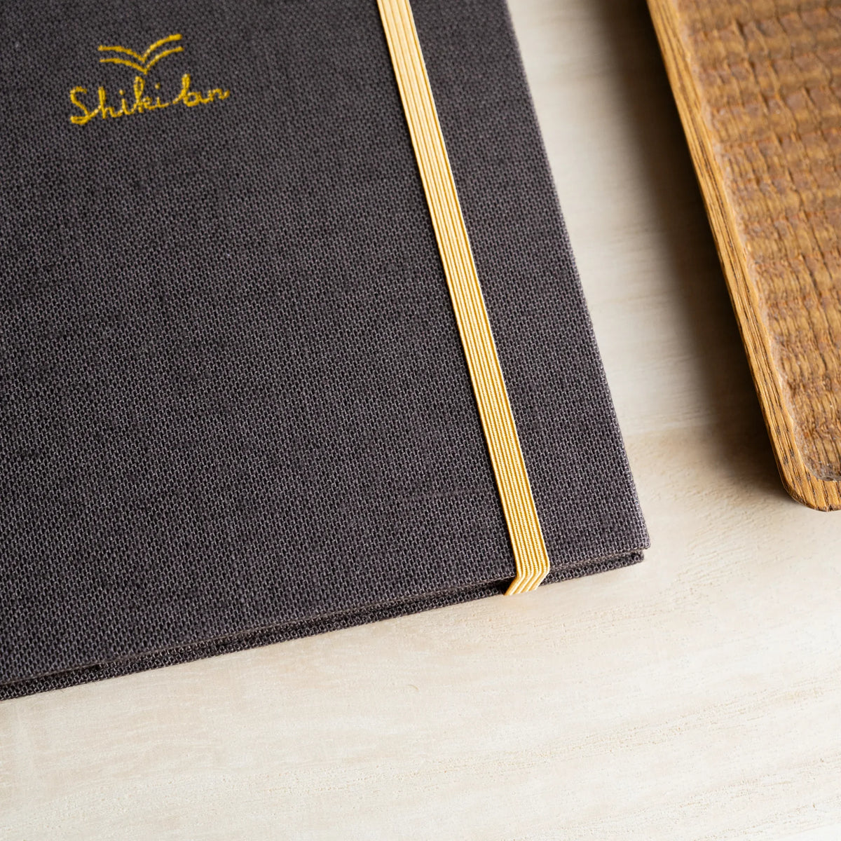 Close-up of the Brown cover, dark brown woven cloth with gold Shiki bun logo and yellow elastic band