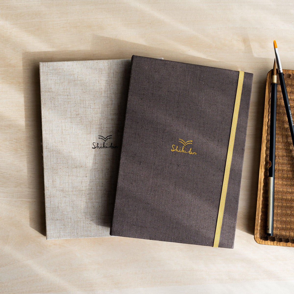 Red Pine Wooden Page Sketchbook in Natural and Brown linen covers with elastic bands, paintbrushes on a wooden tray