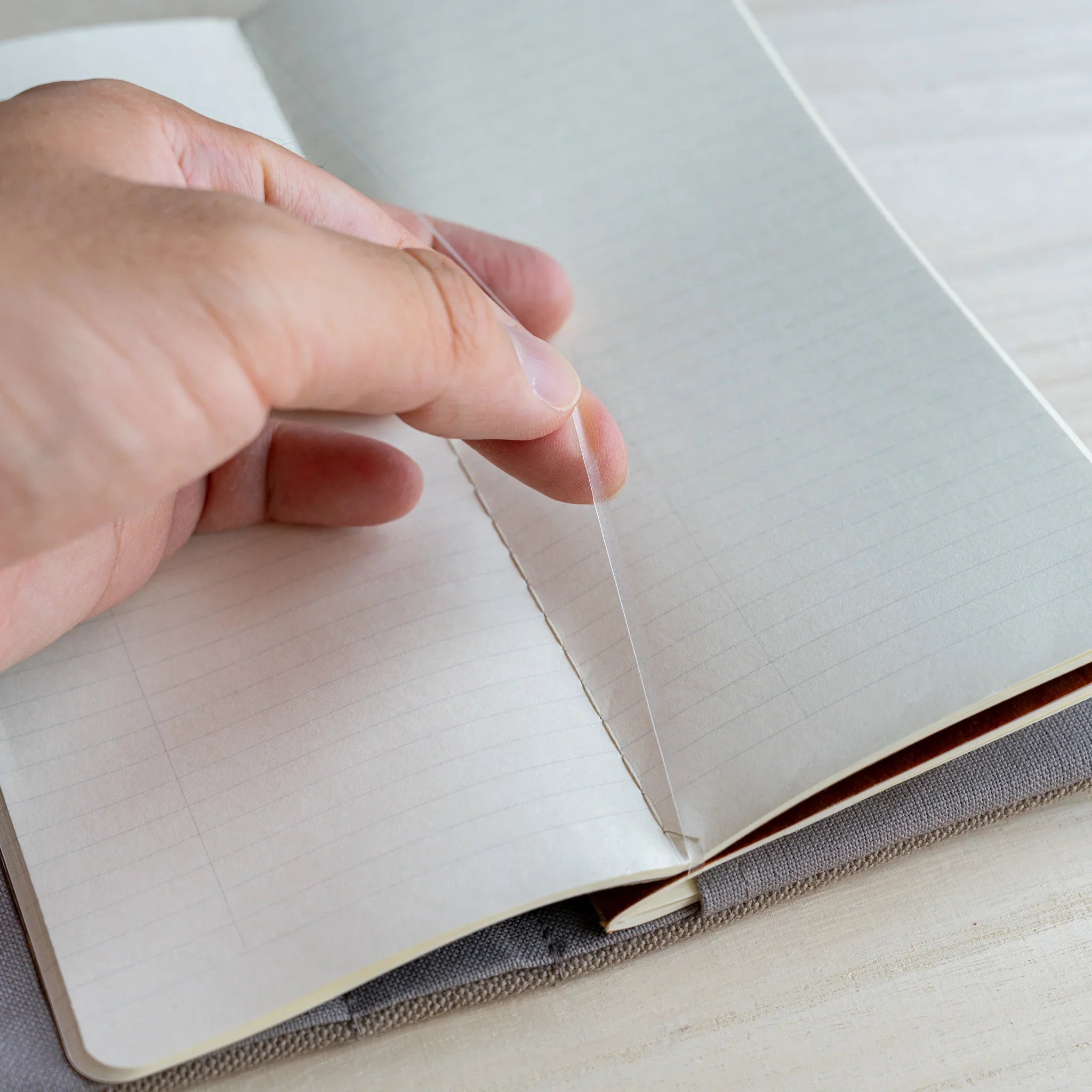 Hand turning a ruled notebook page held inside the RO-BIKI clay beige canvas cover