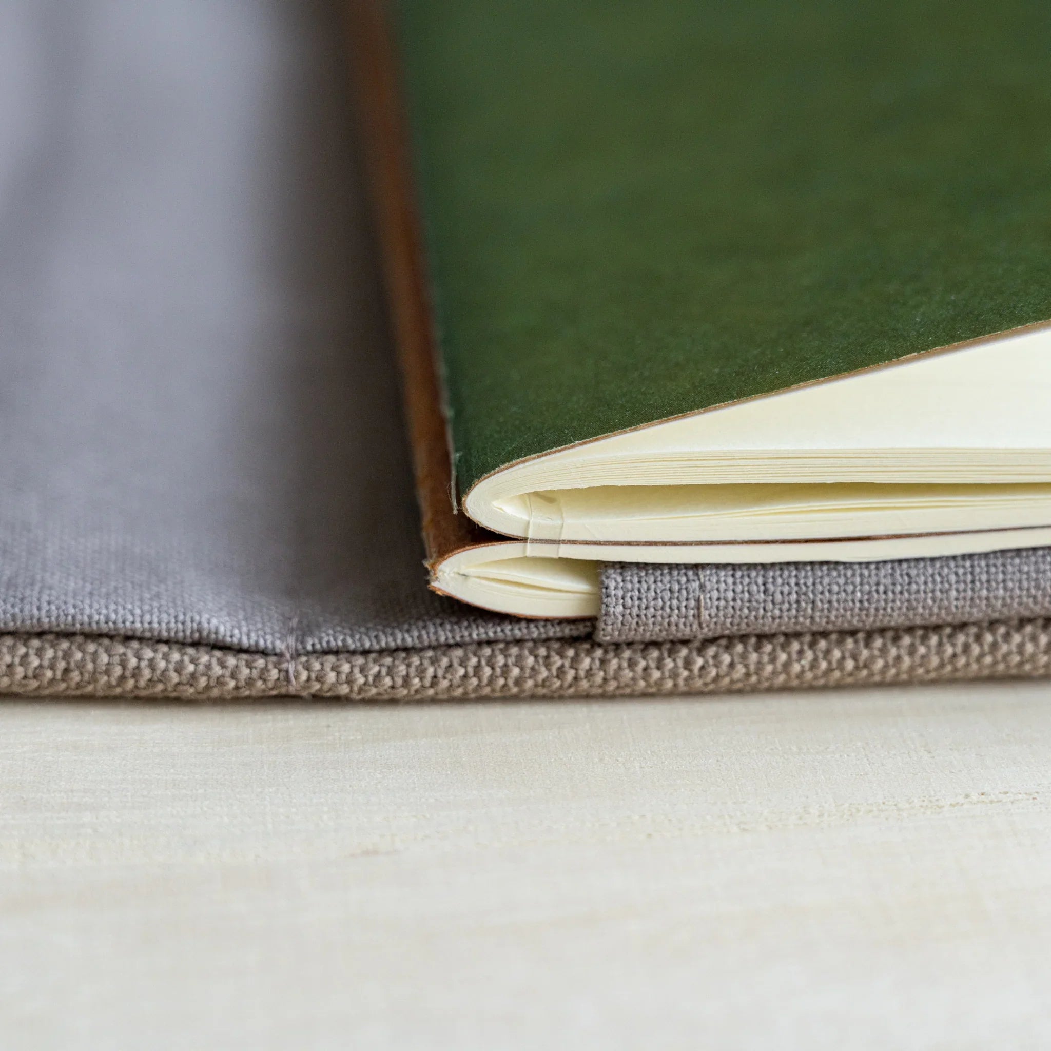 Close-up of a green RO-BIKI notebook with cream pages seated in the clay beige canvas cover