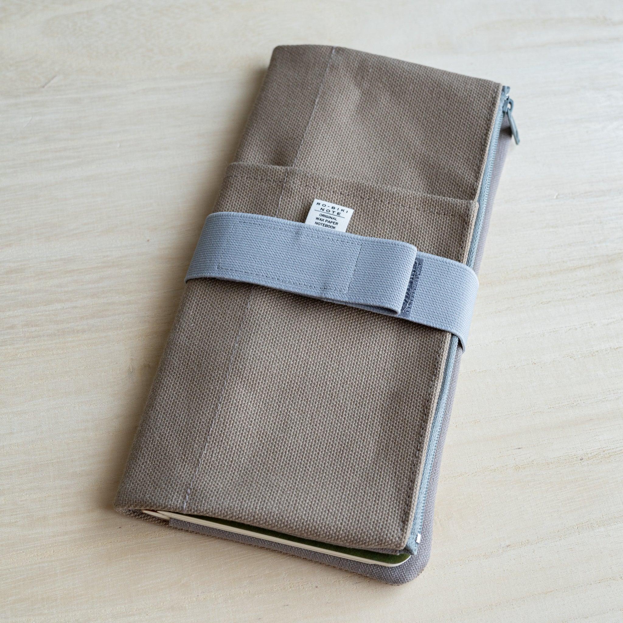 RO-BIKI clay beige canvas cover closed with the pale blue elastic band across the RO-BIKI NOTE fabric tag
