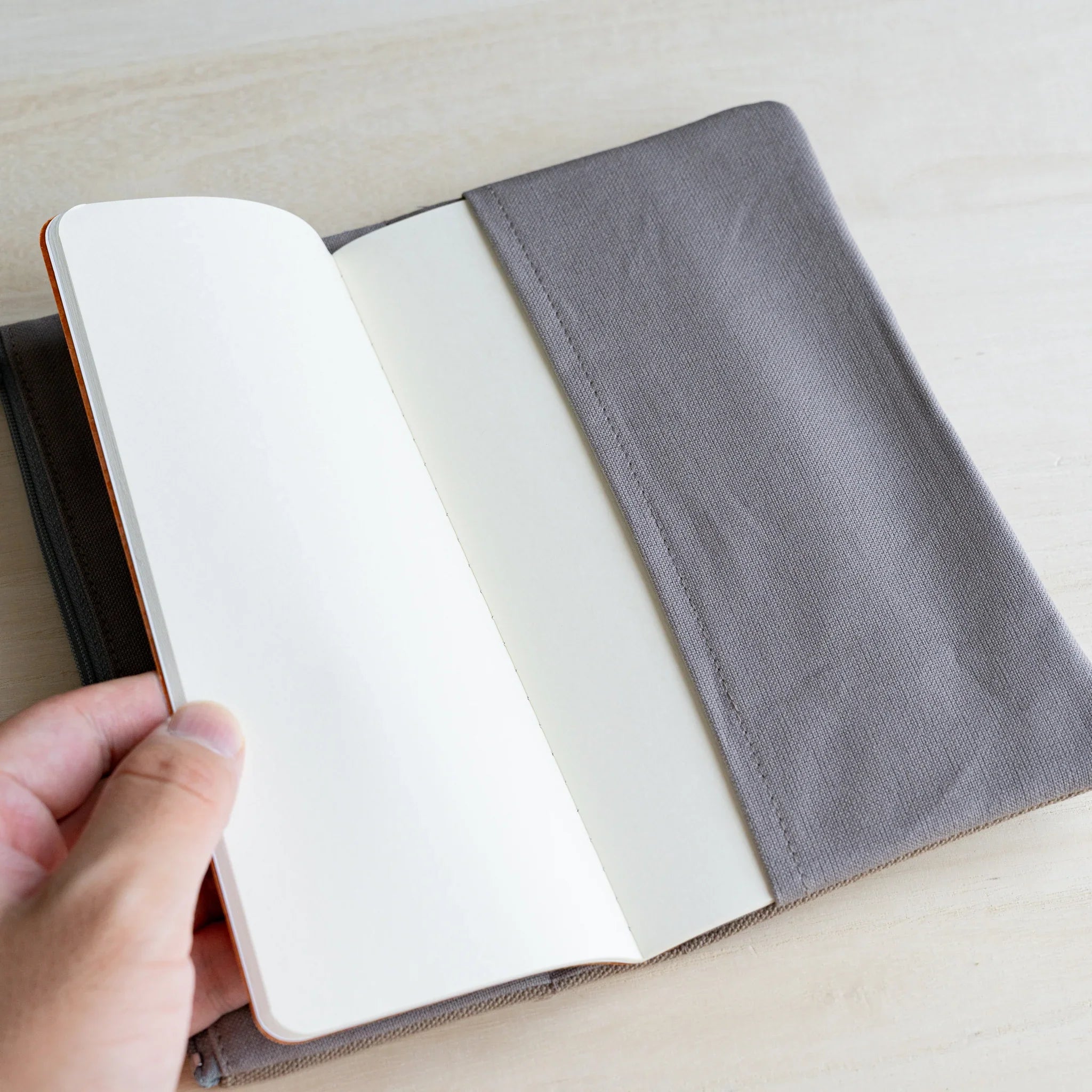 Hand holding a white notebook page inside the grey lined interior of the RO-BIKI clay beige canvas cover