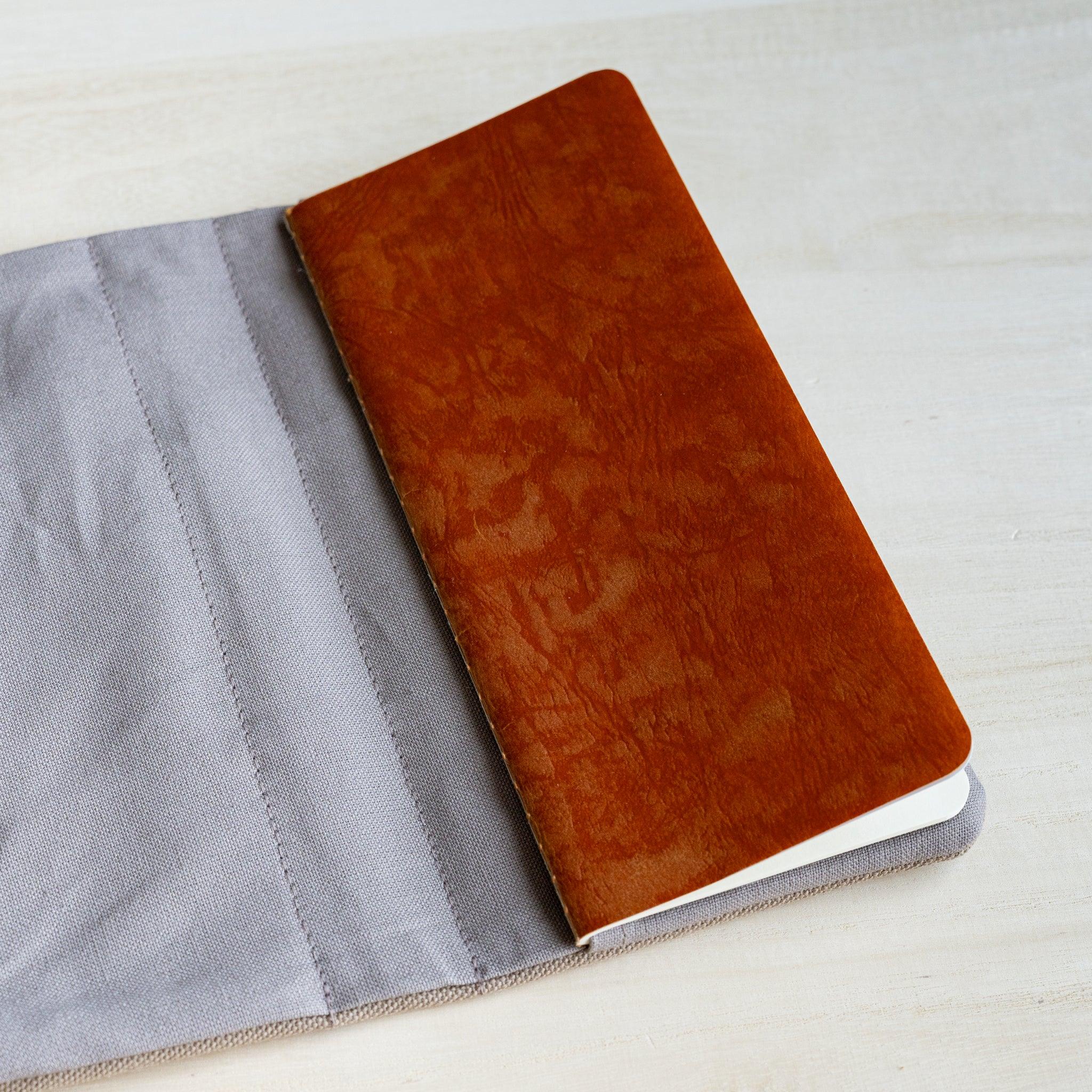 Tan waxed RO-BIKI notebook tucked into the grey inner flap of the clay beige canvas cover