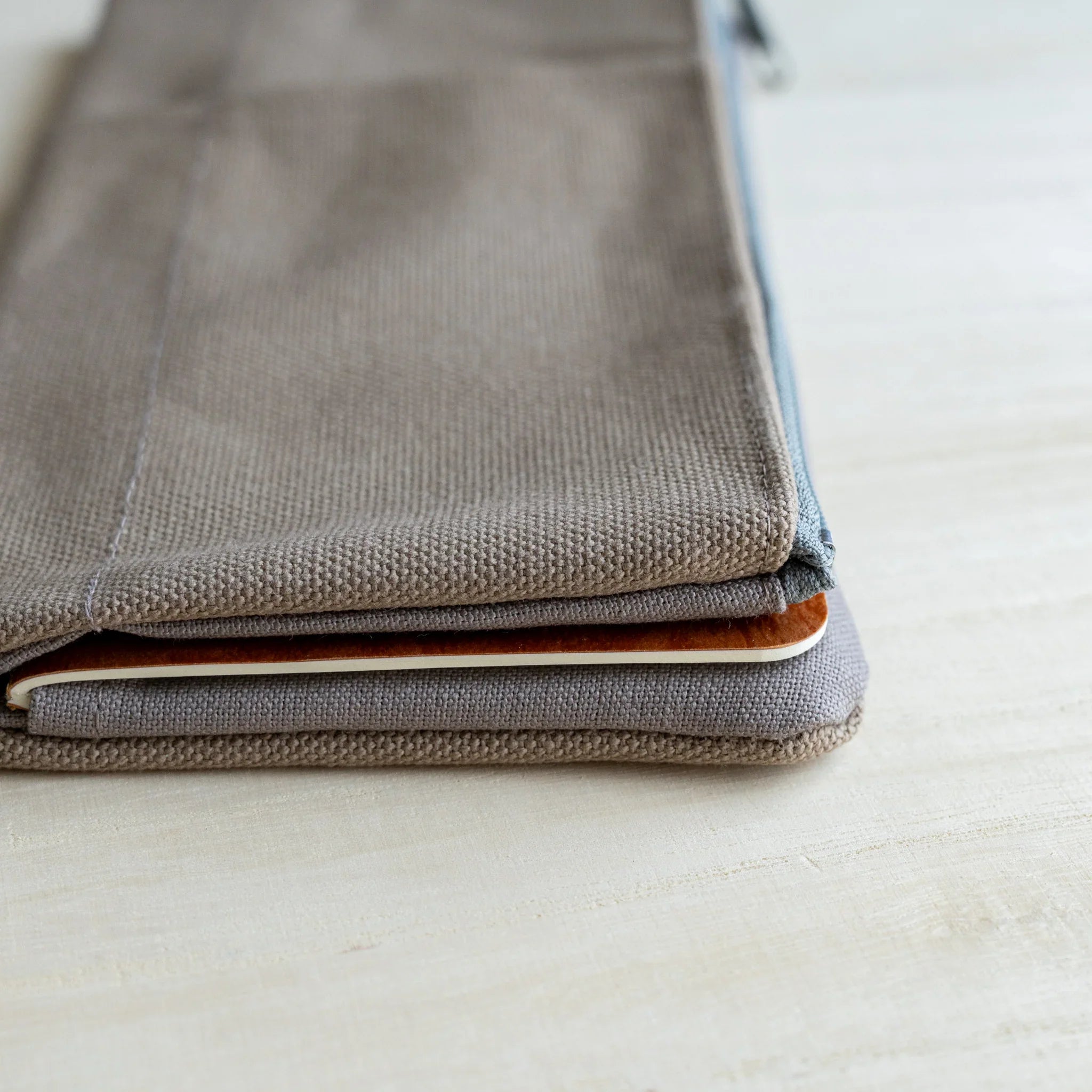 Edge view of the RO-BIKI clay beige canvas cover closed over a notebook, showing the canvas weave