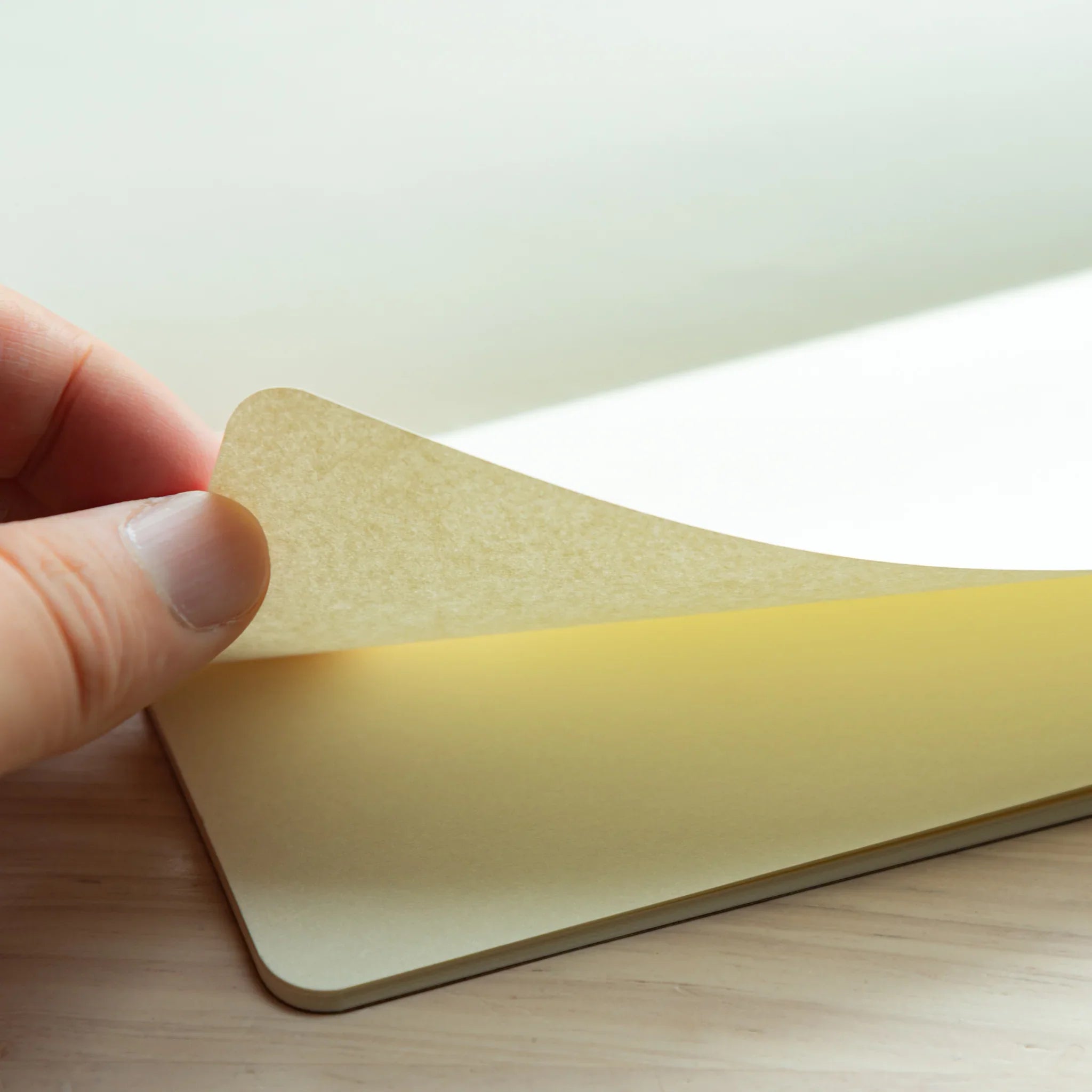 Hand lifting a blank cream page of the RO-BIKI Star Map Notebook, showing smooth textured paper with rounded corner.