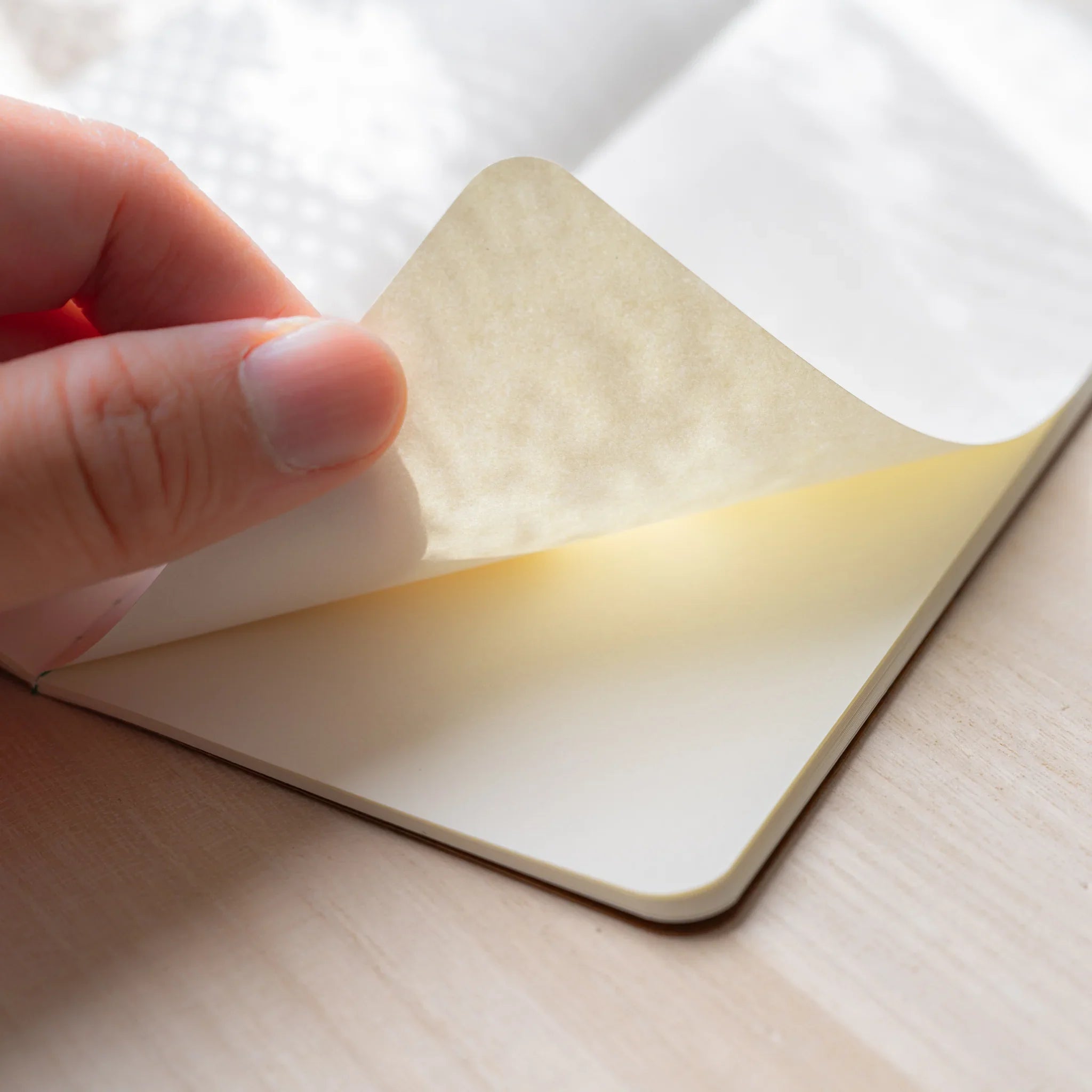 Hand lifting a page of RO-BIKI NOTE showing the thin translucent New Chiffon Cream paper texture and quality