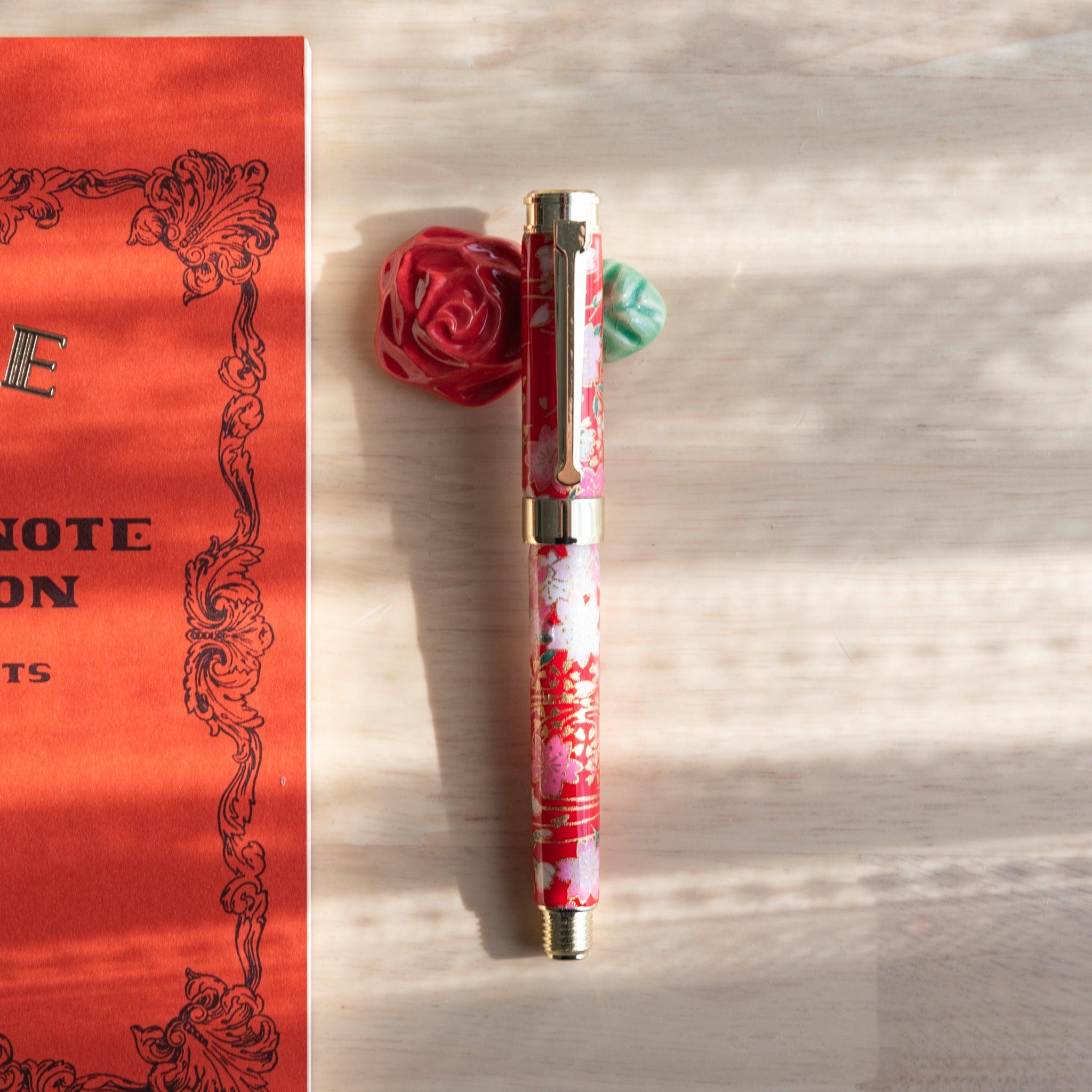 Red ceramic pen rest with a green leaf, paired with a floral-patterned fountain pen, showcasing Japanese stationery.