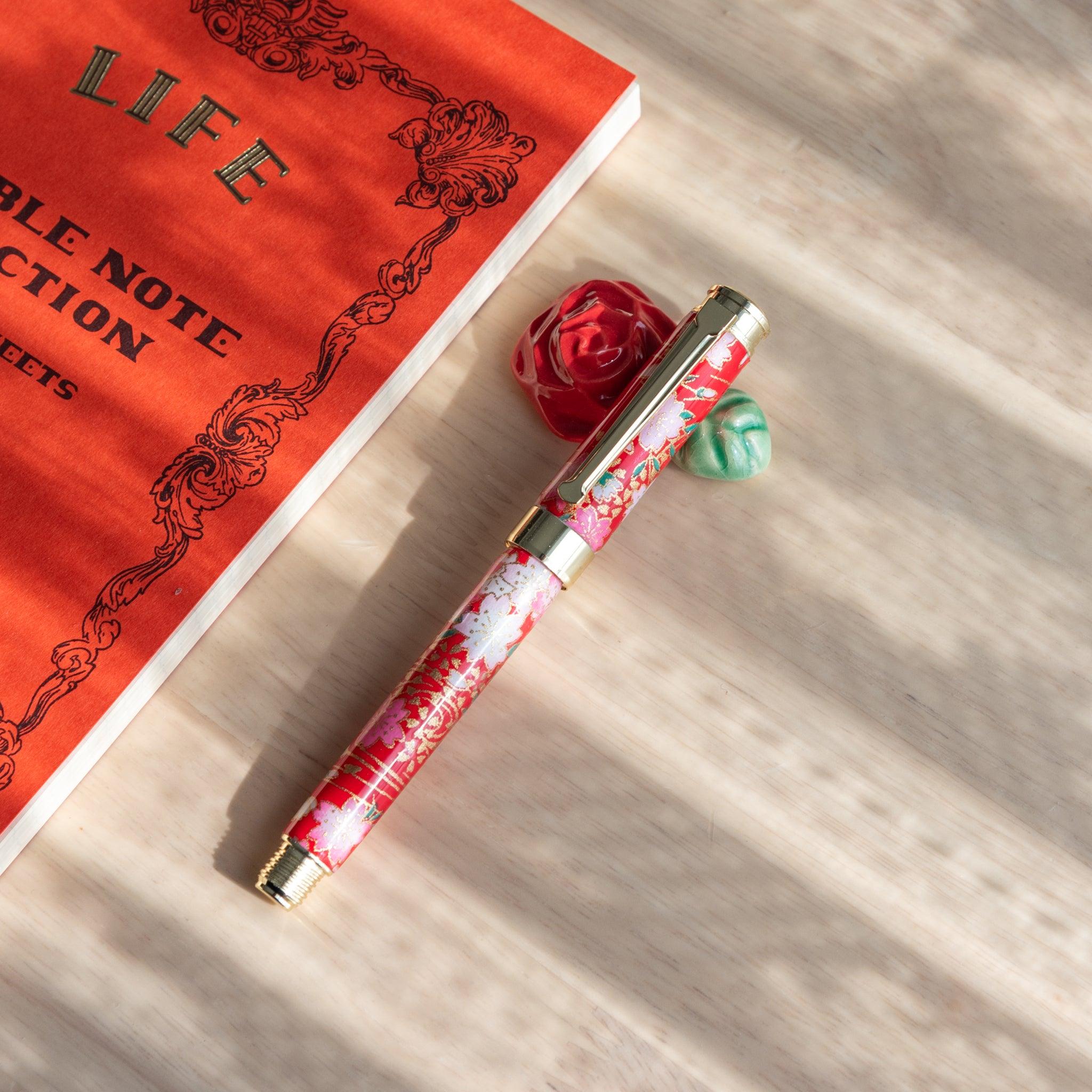 Red ceramic pen rest with a green leaf, paired with a floral-patterned fountain pen, showcasing Japanese stationery.