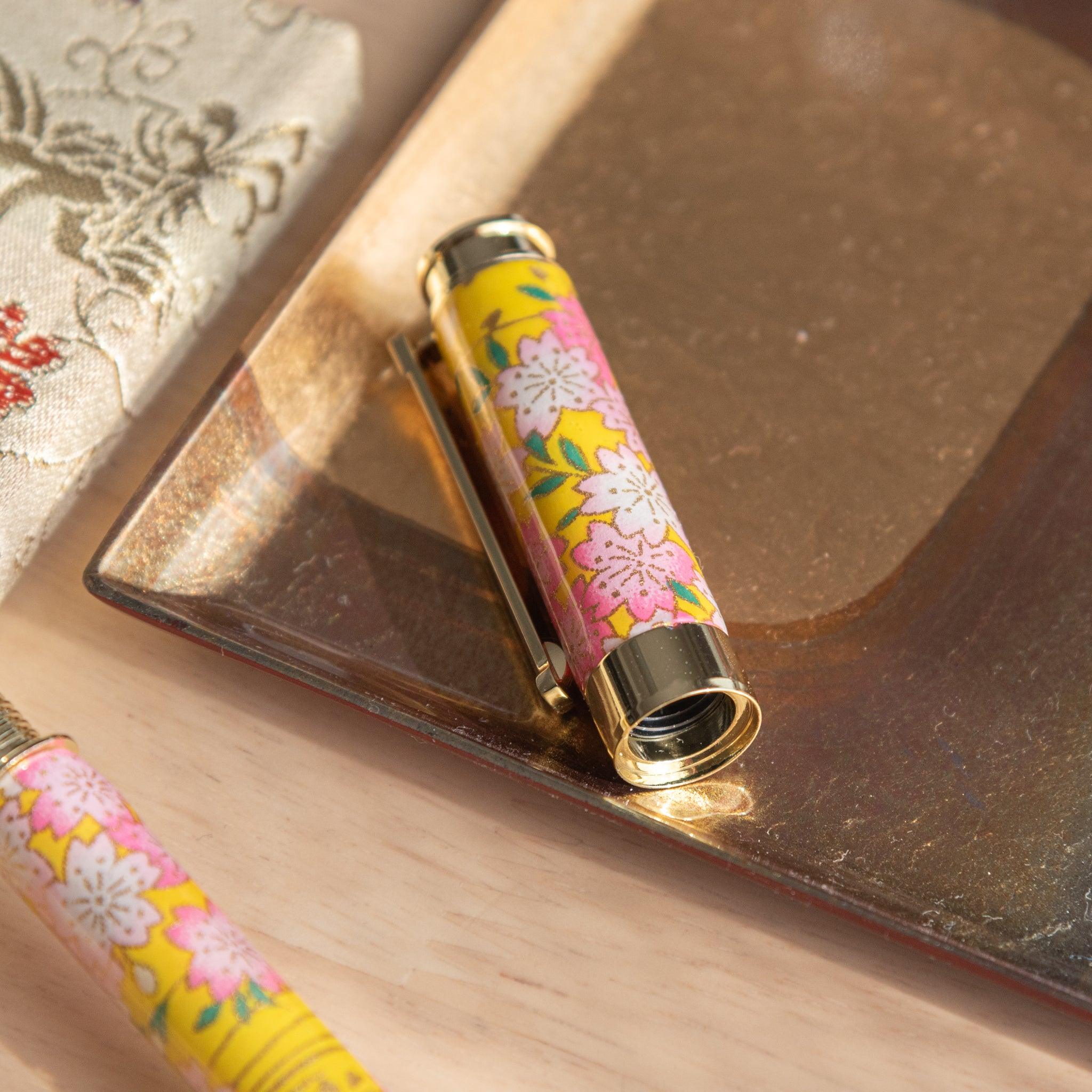 Japanese fountain pen cap featuring a sakura and canola design in bright yellow, placed on a golden tray. (84 characters)