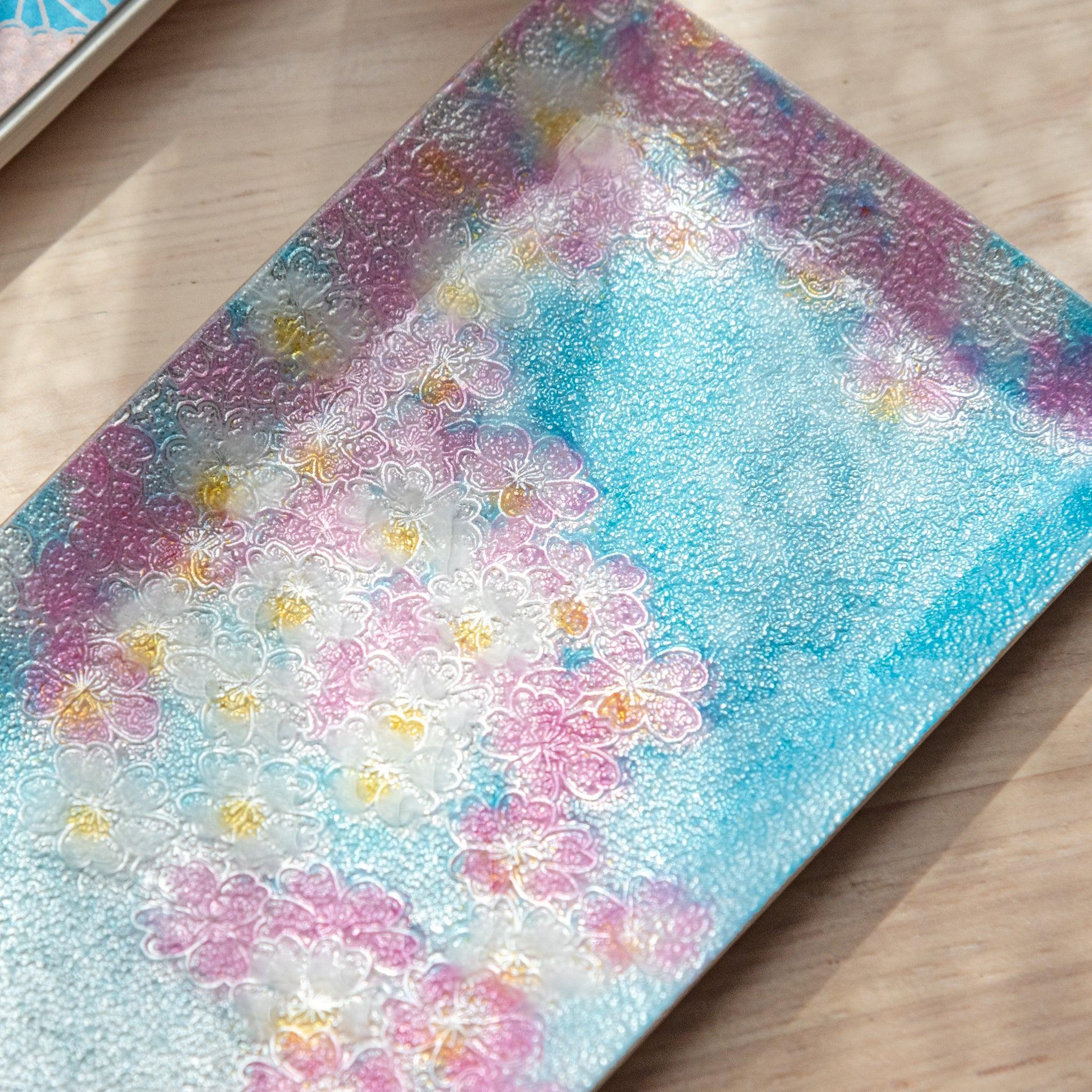 Close-up of a tray with intricate cherry blossom pattern in pink and white, set against a textured blue background, highlighting delicate petal details.