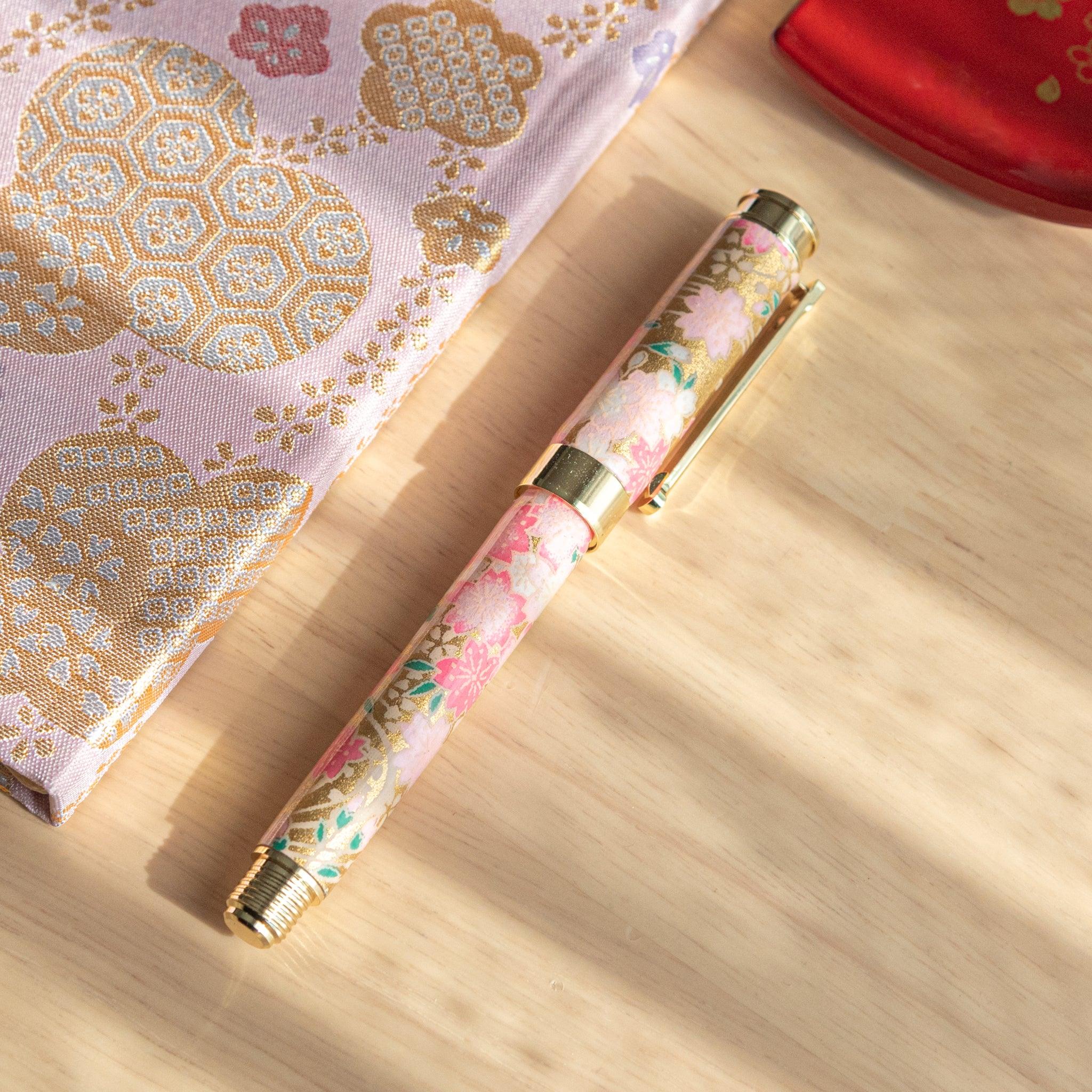 Closed sakura-themed fountain pen with gold accents, placed on intricate golden-patterned fabric in soft light. (96 characters)