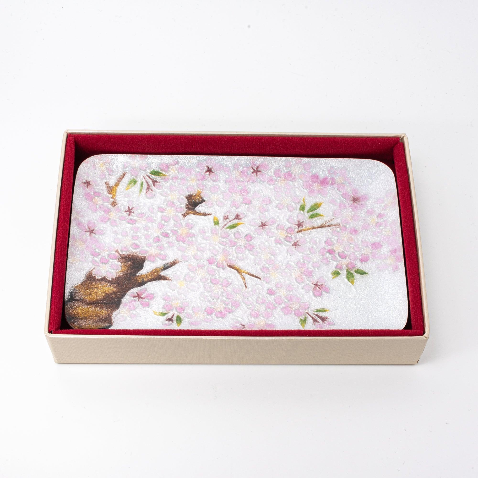 Silver tray featuring pink cherry blossoms and brown branches, presented in a red-lined beige gift box.  