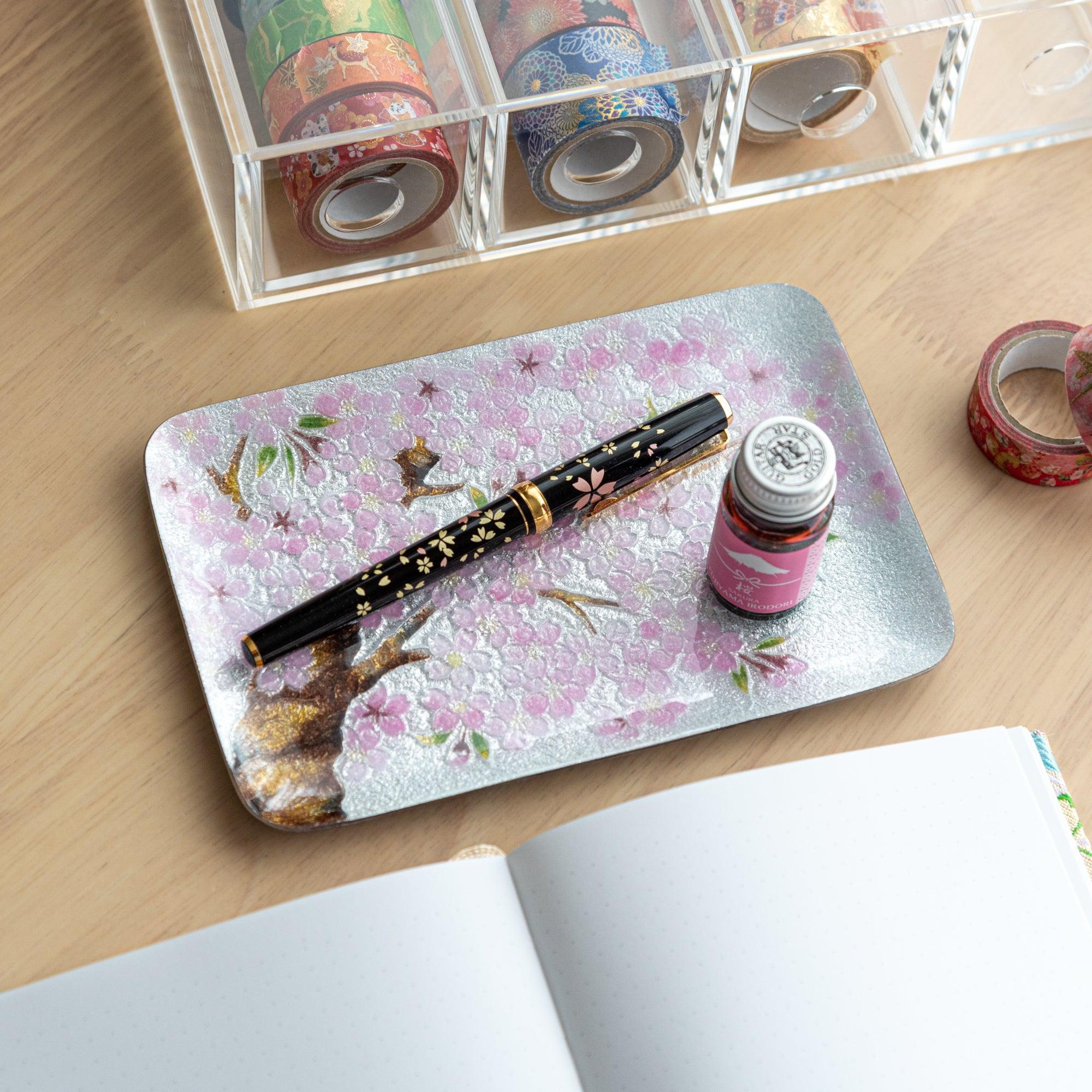 Tray featuring pink cherry blossoms with a black floral fountain pen and pink ink bottle placed on top for an artistic display.  